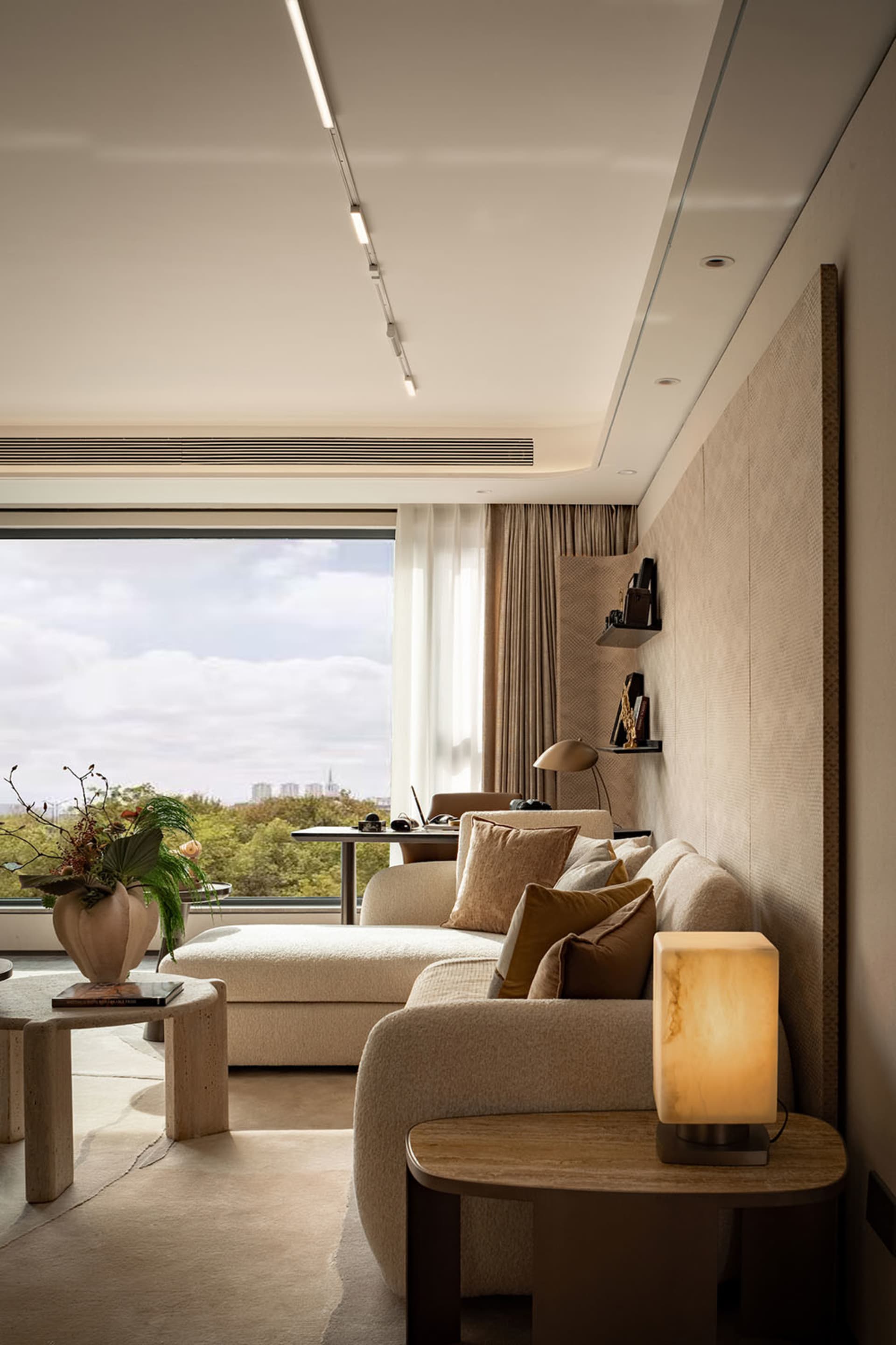 A city-view living room with two couches, a chair, a dining table, potted plants, and a vase, set against a backdrop of a large window and a cityscape outside