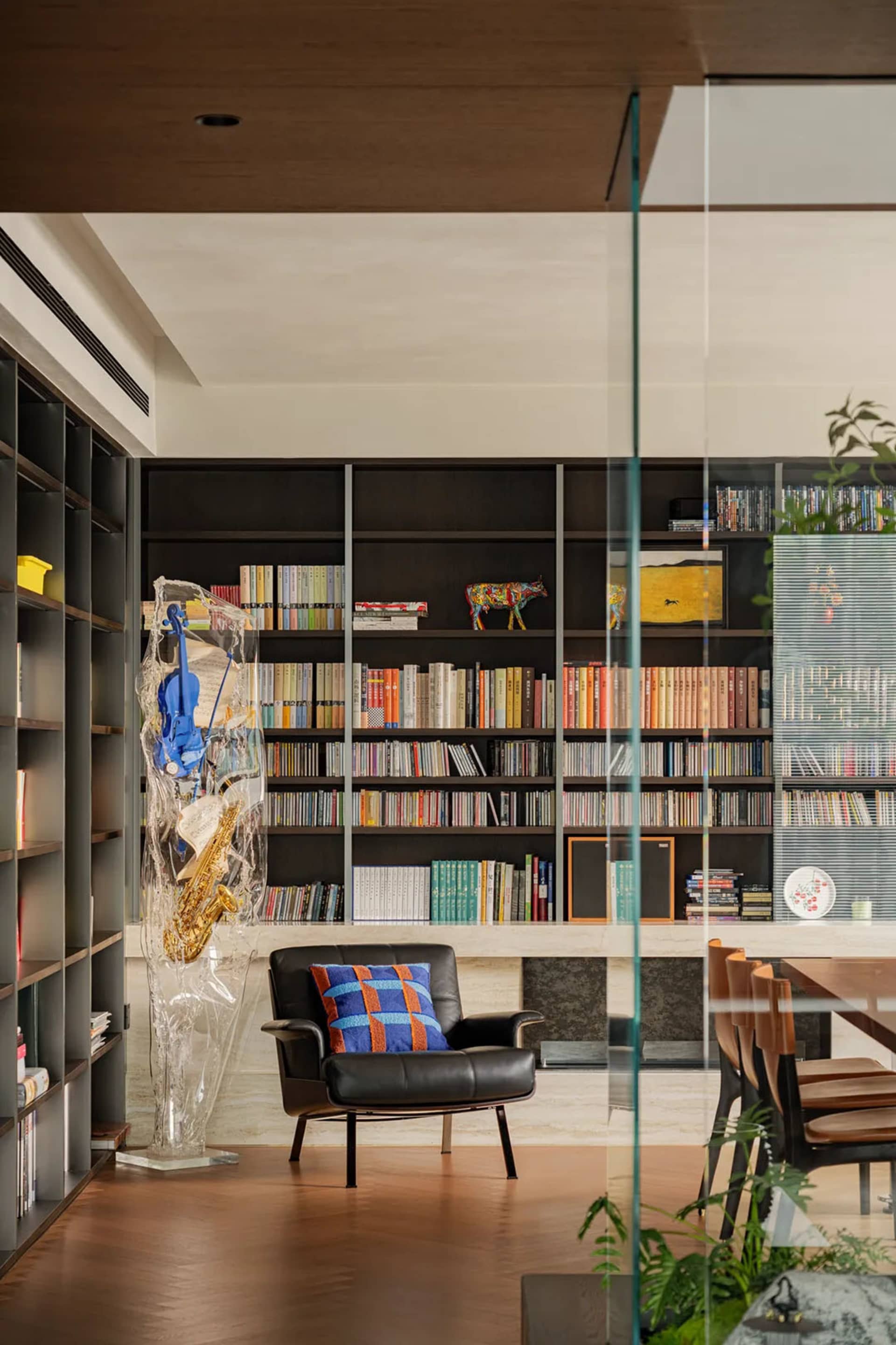 Modern living room with a black leather chair, glass walls, and bookshelves, featuring a clean and minimalist design with natural light and a luxurious atmosphere