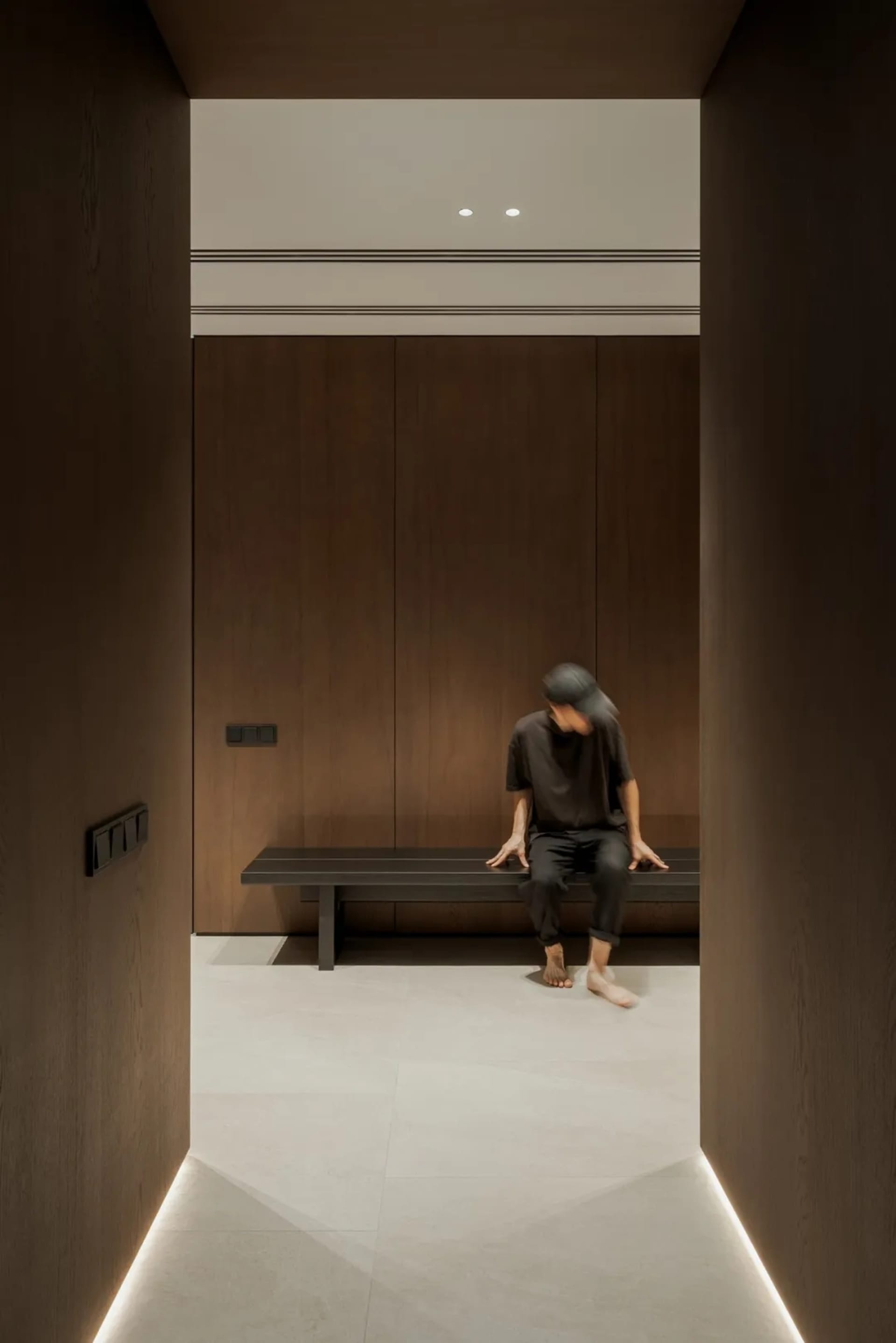 A man sits on a bench in a dark room with wooden walls and flooring, giving it an old and rustic feel