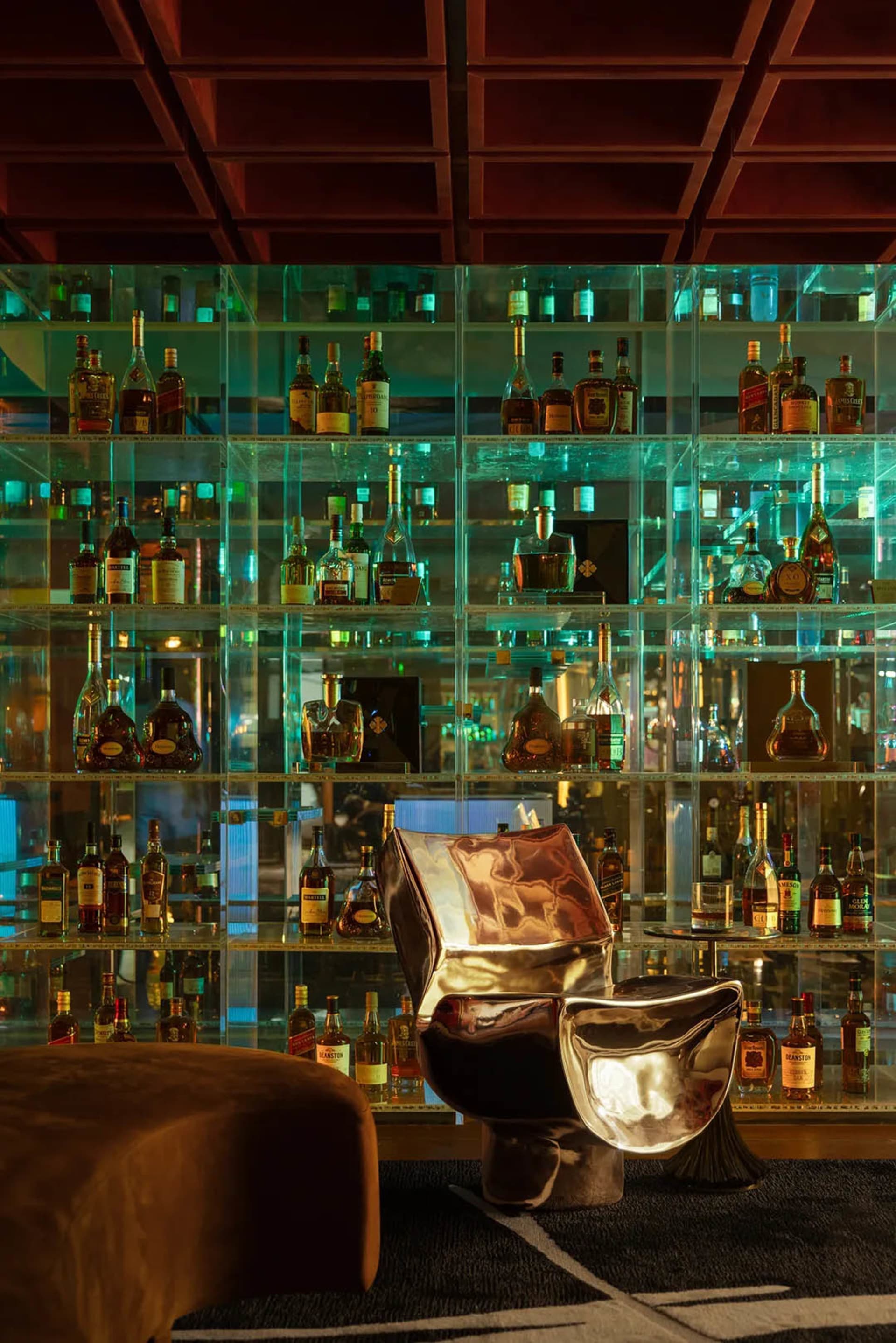 A cozy bar area with glass shelves displaying a collection of liquor bottles and a chair for seating, set in a relaxed environment