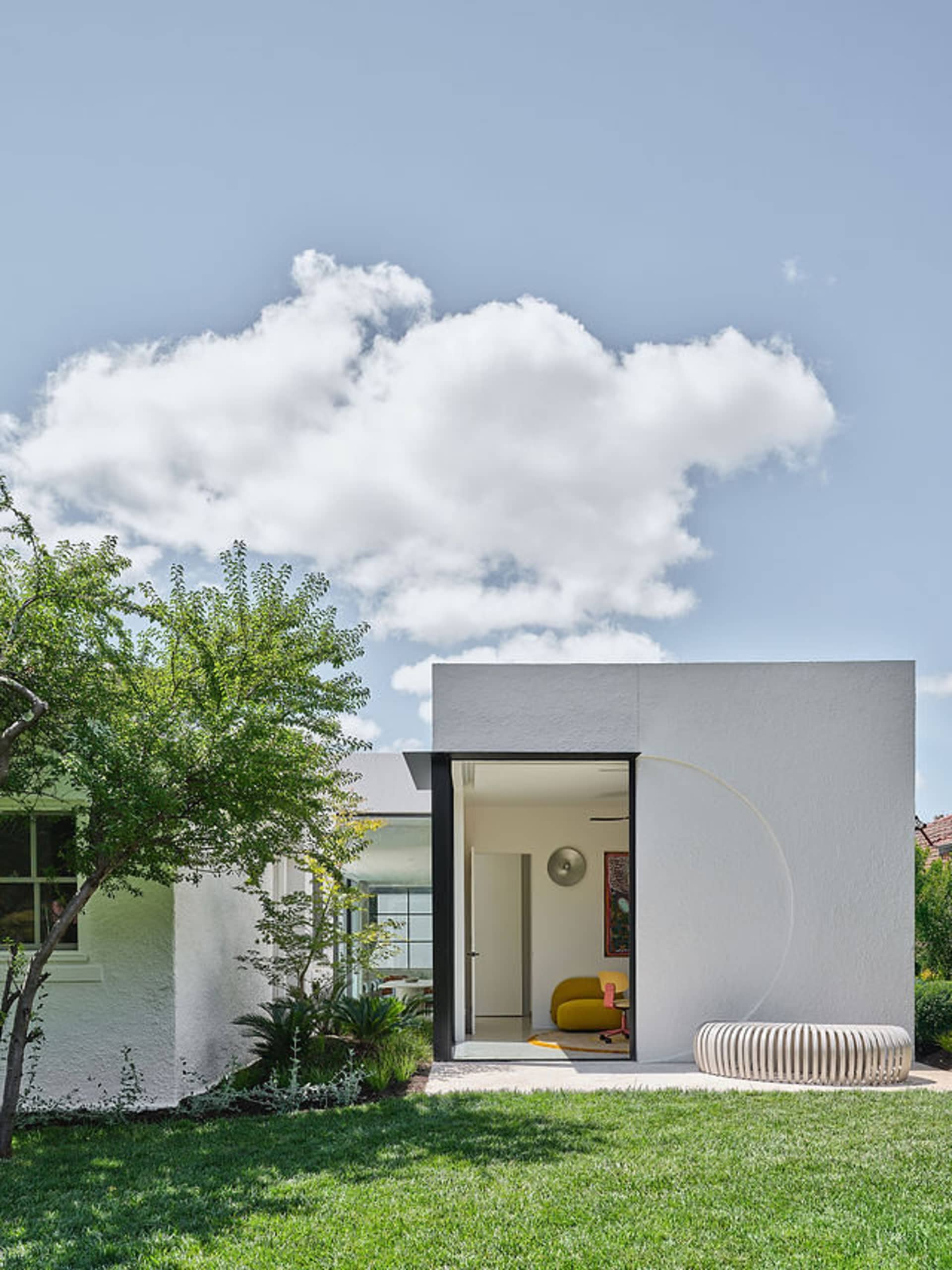 Open living area with a white wall divider, a yellow couch, potted plants, and natural light through windows