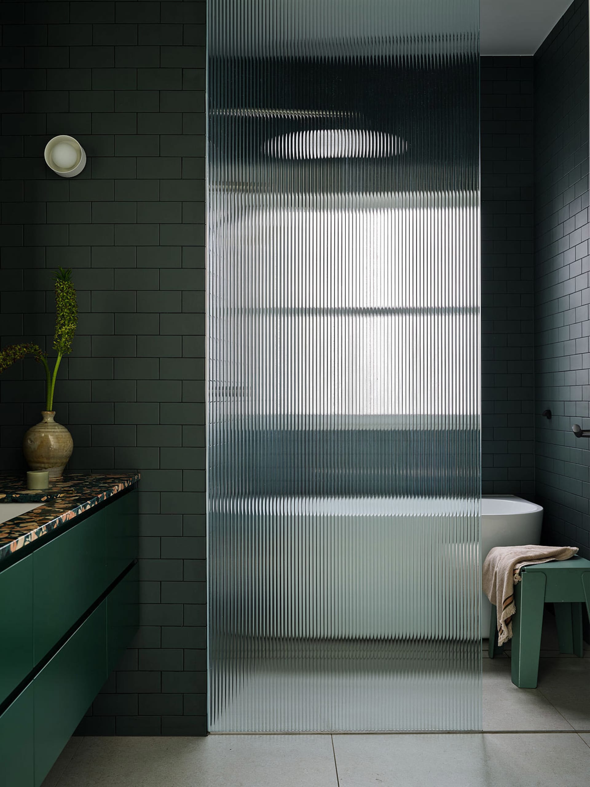 Modern bathroom with black walls, a tile floor, a glass shower door, a sink, and a bathtub, decorated with a vase on the countertop
