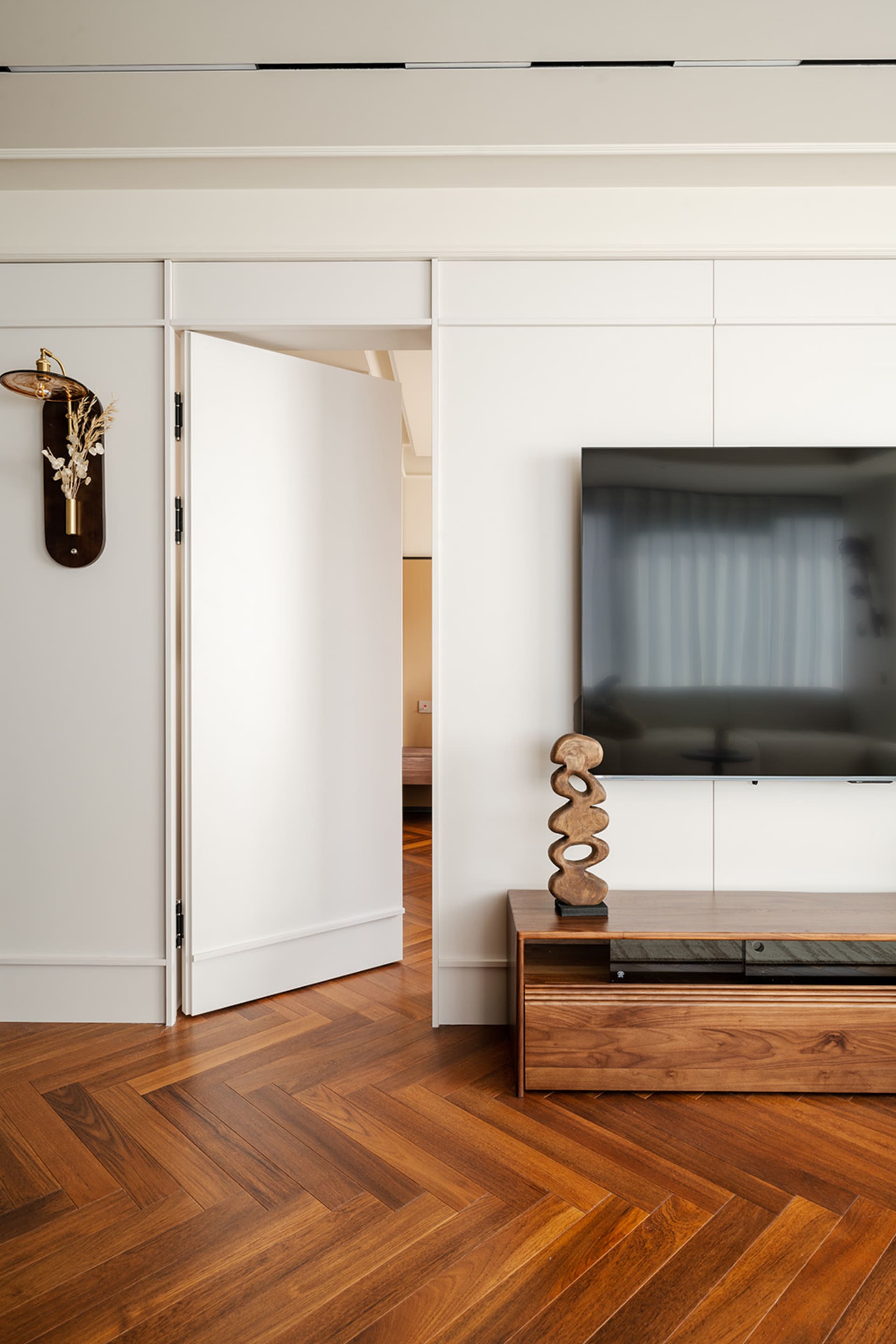 A modern living room with hardwood floors, white walls, a large flat screen TV, and a chair and two couches arranged in a contemporary style