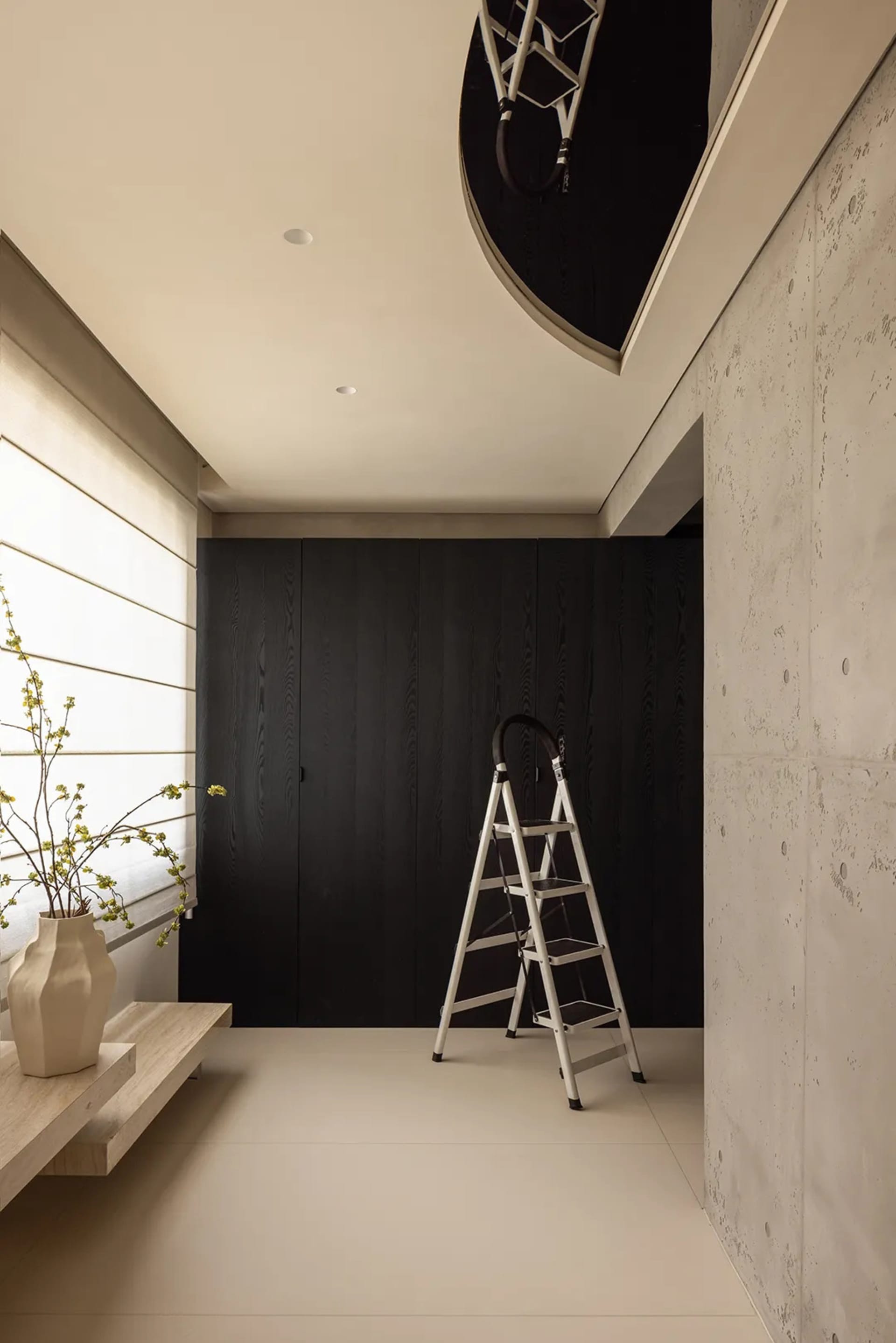 A clean and organized living area with a white wall, a black doorway, and a vase near the bottom left corner, featuring two ladders and a sense of minimalism