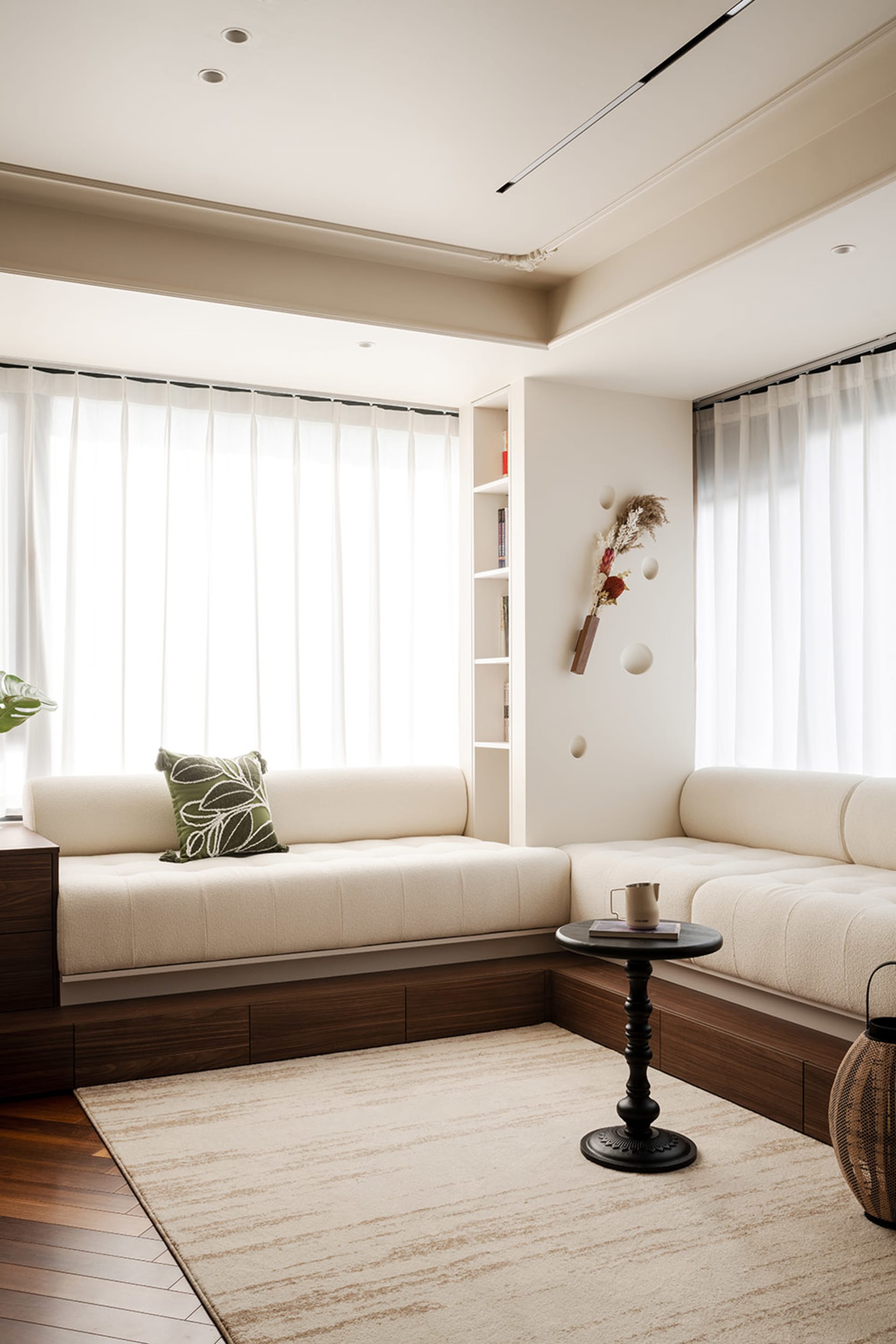 Cozy living room with a couch against a white wall, natural light from two windows, and wooden floors, with a potted plant adding a touch of greenery