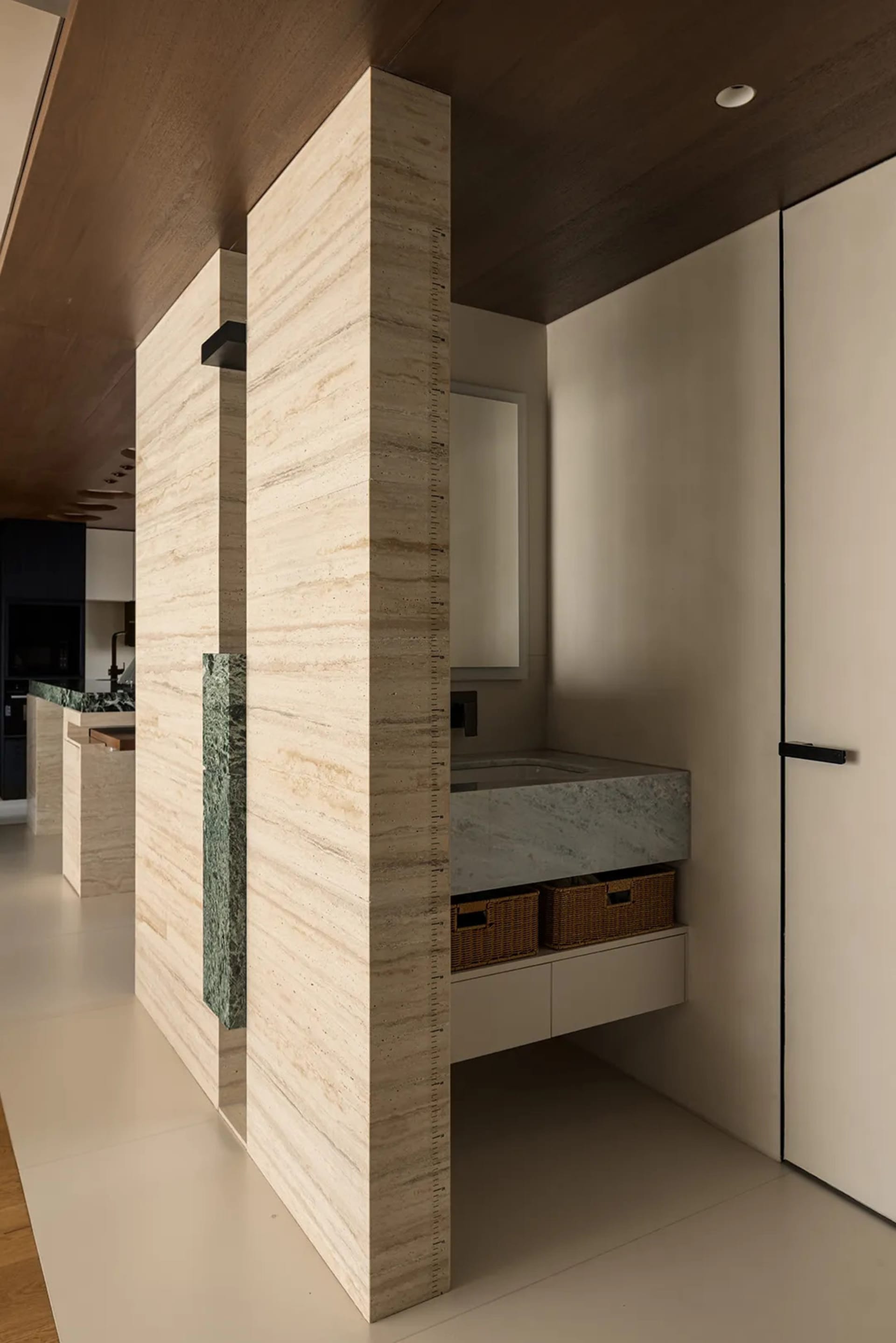 Bathroom with marble walls, sink, mirror, and shower area, featuring modern and sophisticated design with warm and inviting lighting