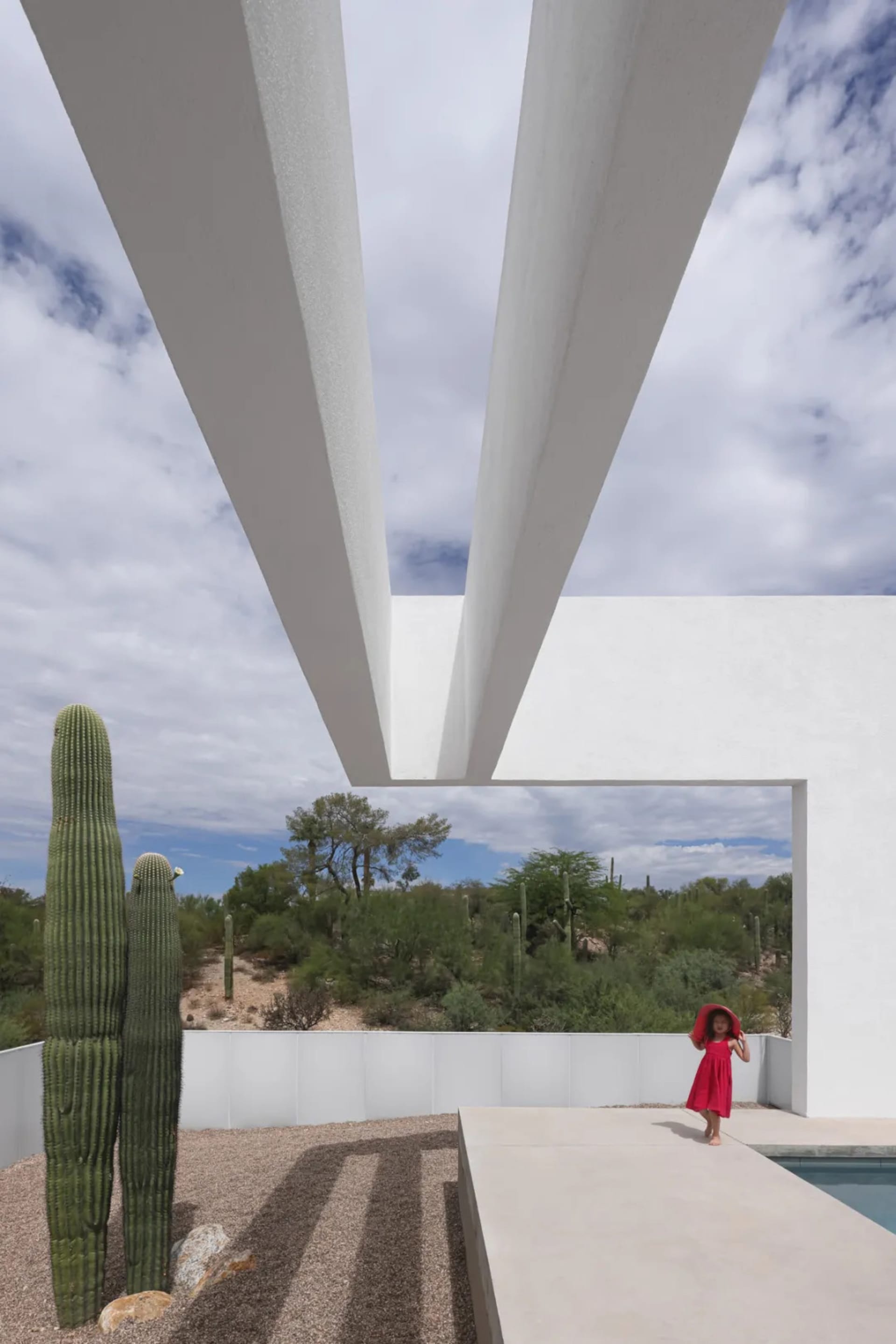 Modern desert building with a bridge-like structure, surrounded by cacti and a person in the foreground