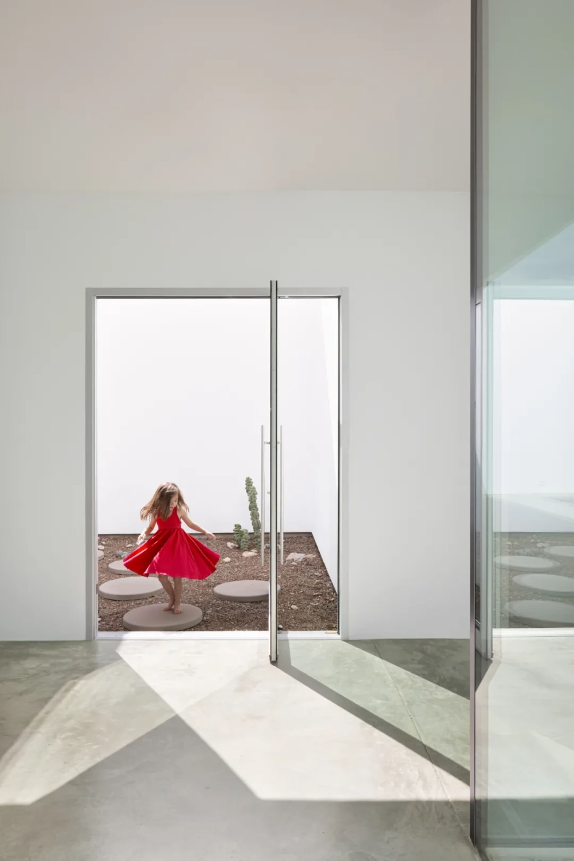 A young girl in a red dress spins around in a room with hardwood floors, two doors, and three bowls, creating a playful and joyful atmosphere