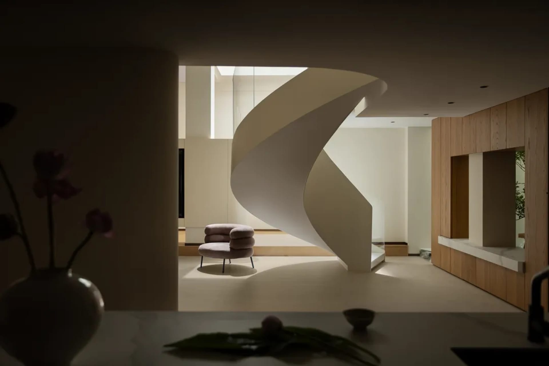 Modern living space with a spiral staircase made of wood, a chair, and a vase, set against a neutral background