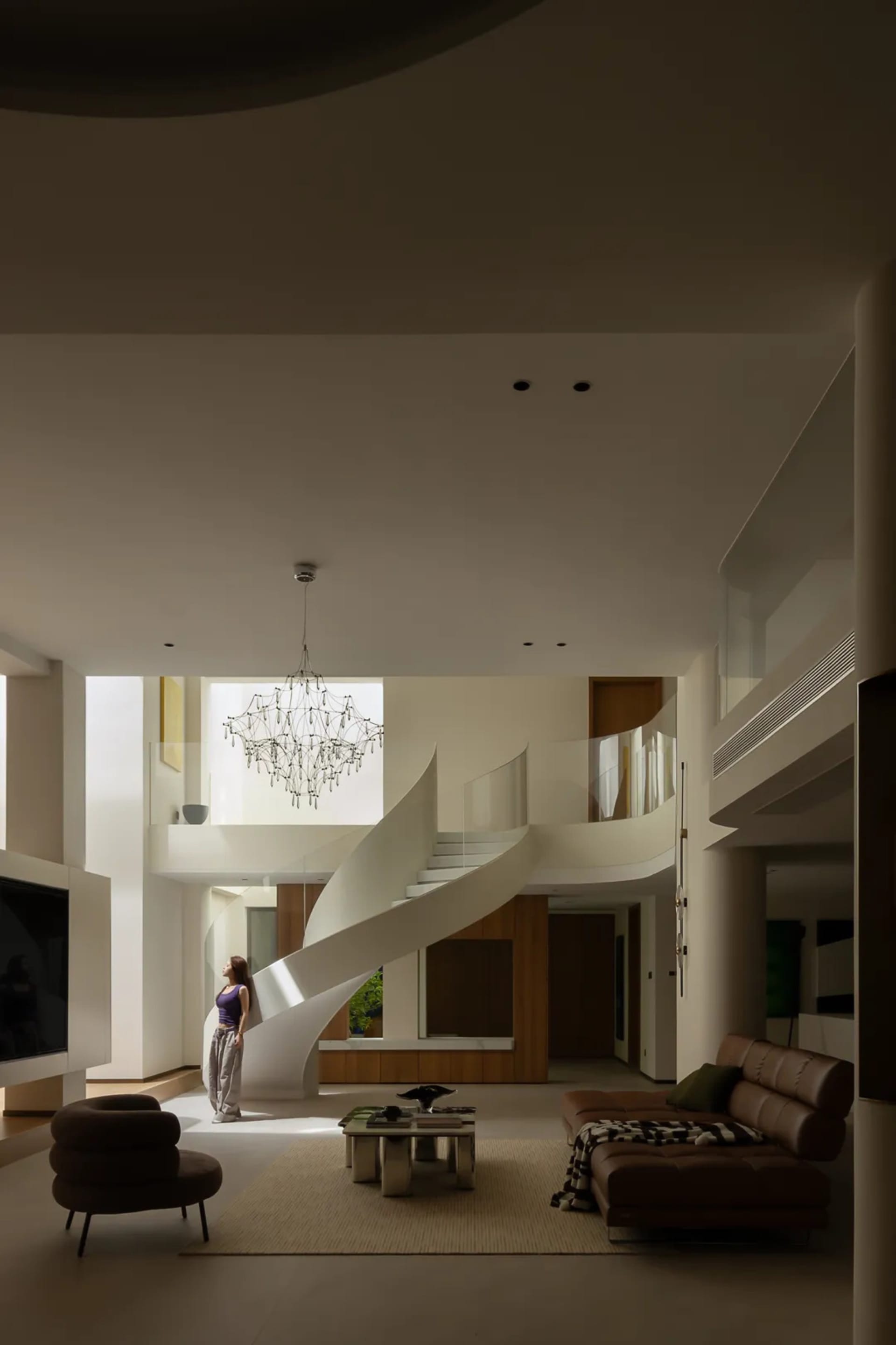 Open concept living space with a spiral staircase, two couches, a chair, and a woman standing at the bottom of the stairs