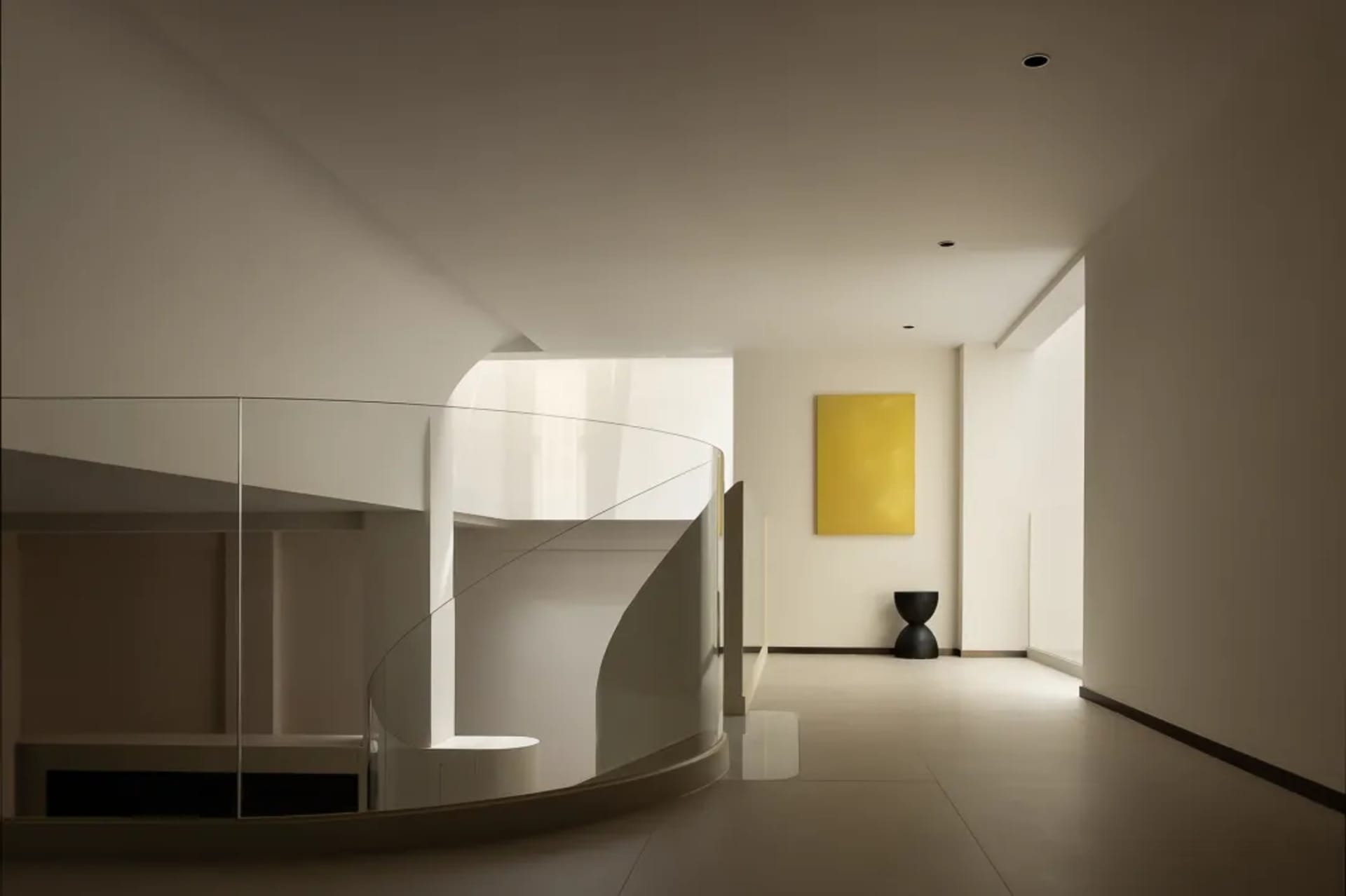 Open living area with a glass spiral staircase, white walls, a painting, and a vase, creating a modern and minimalist atmosphere
