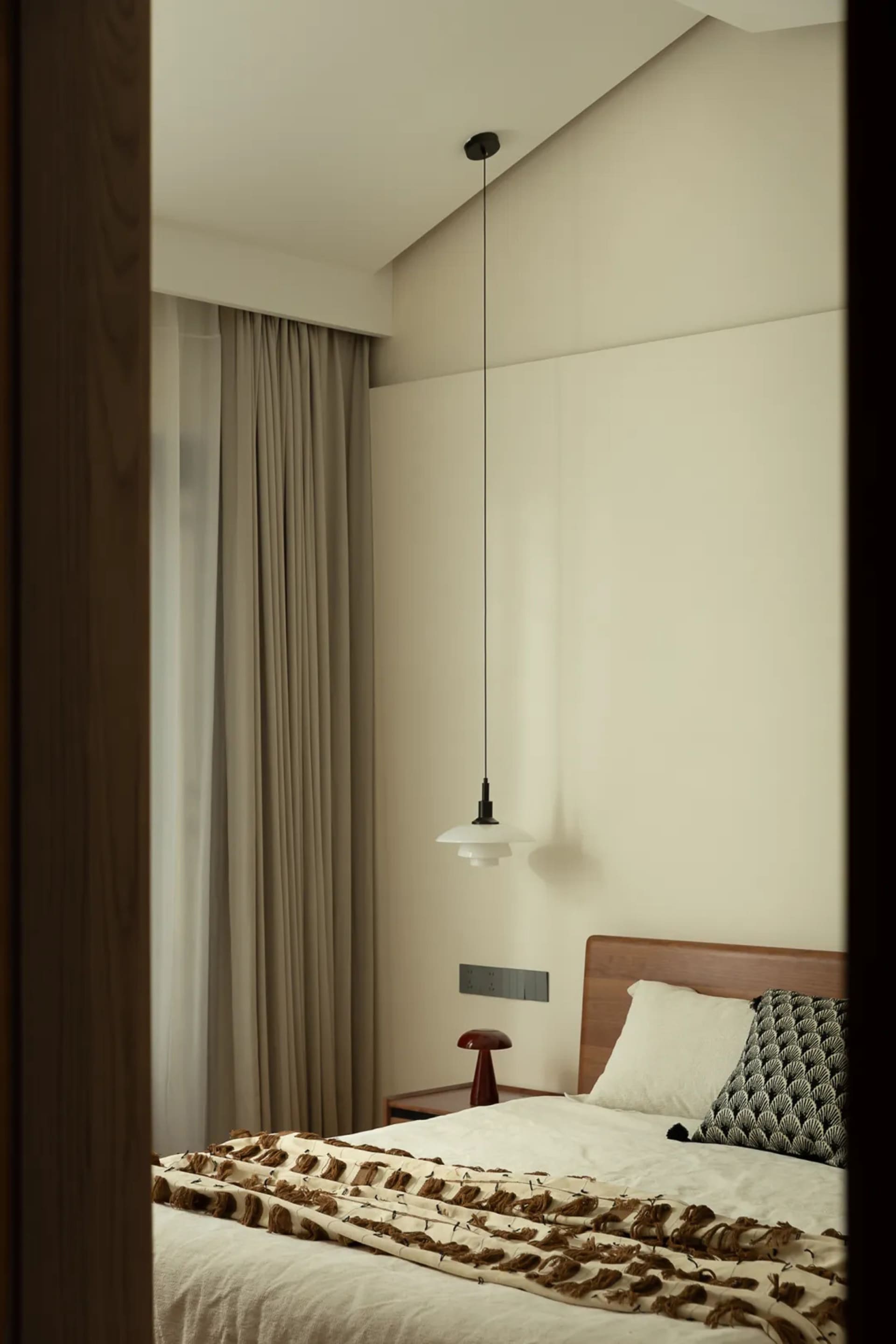 A serene bedroom with a white wall, wooden headboard, and a chair, featuring a cozy bed setup with two pillows