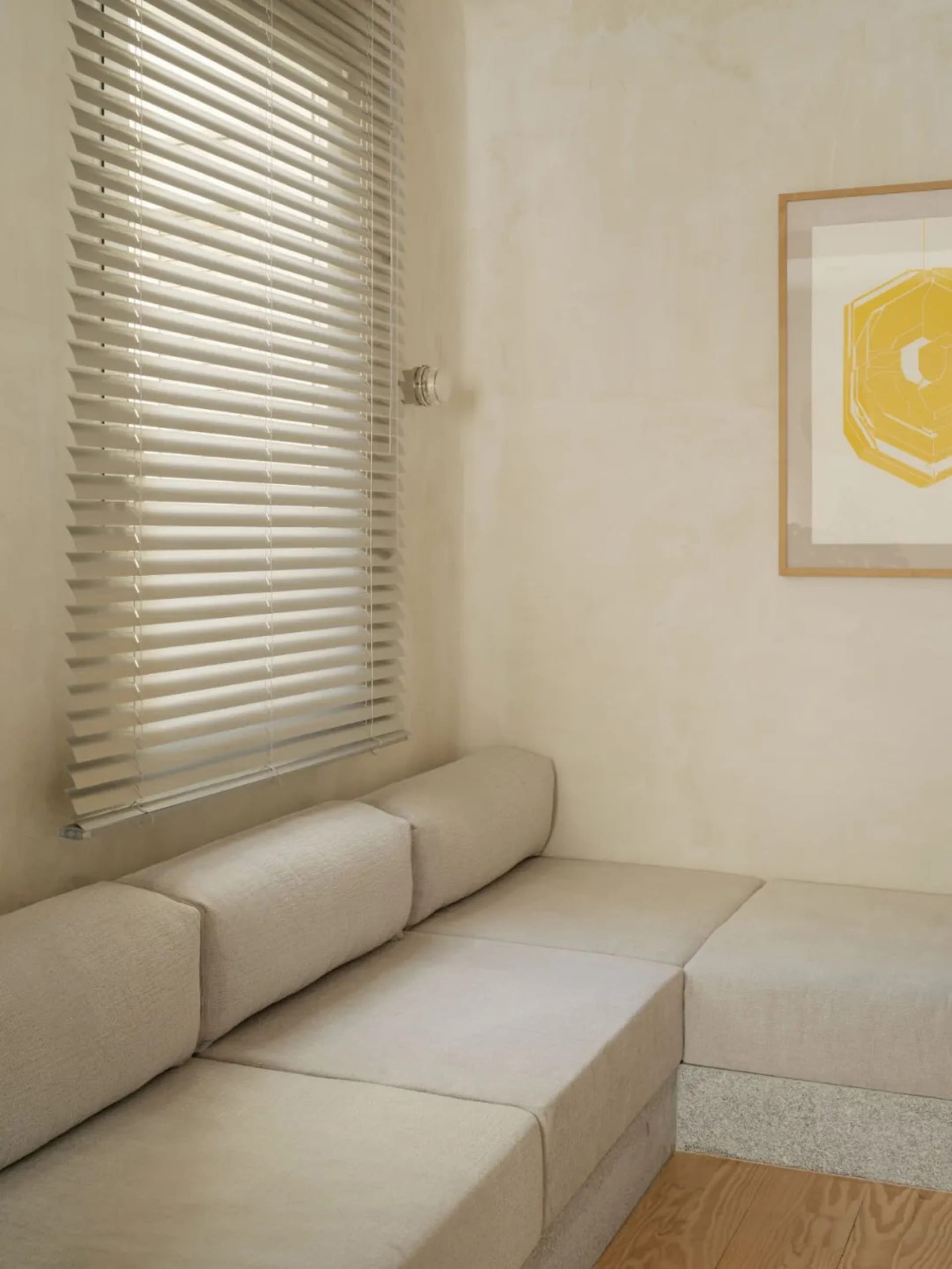 A living room with a couch and bench next to each other, surrounded by white walls, two windows, and wooden furniture