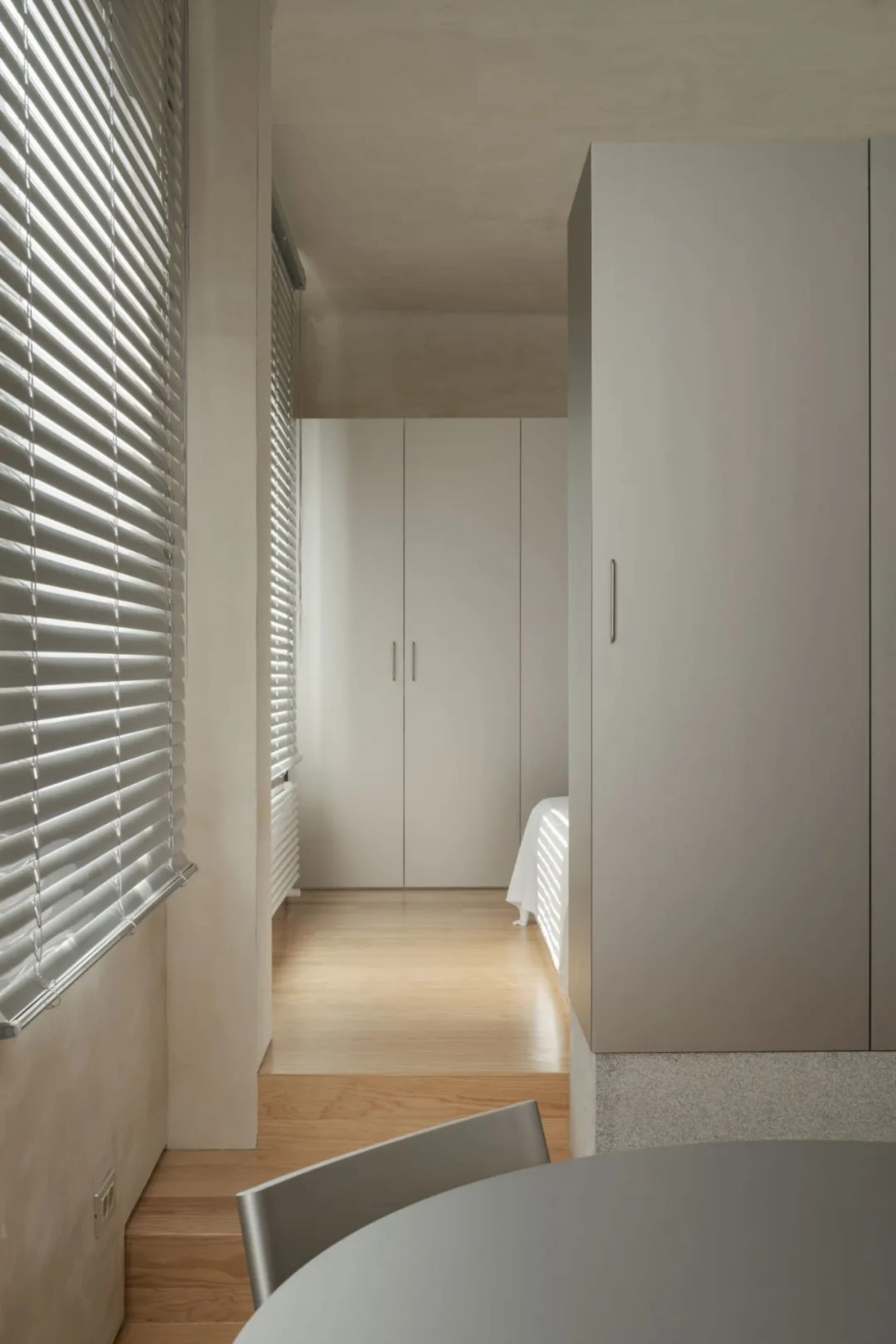 Cozy small bedroom with wooden floors and white walls, featuring two beds and a chair in a inviting atmosphere