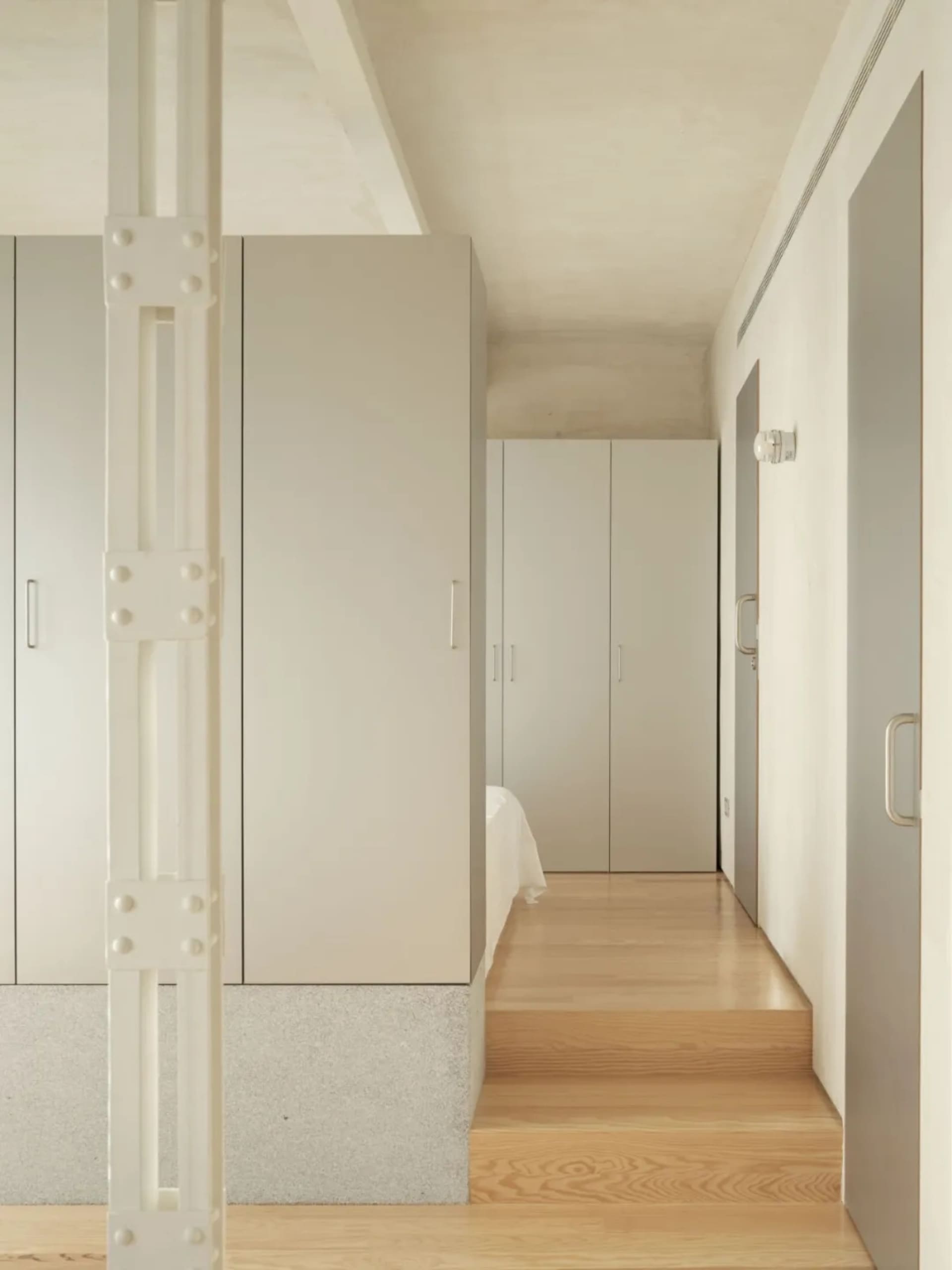 A calm and inviting bedroom with white walls, wooden floors, and a large bed positioned towards the right side of the room, accompanied by two large closets