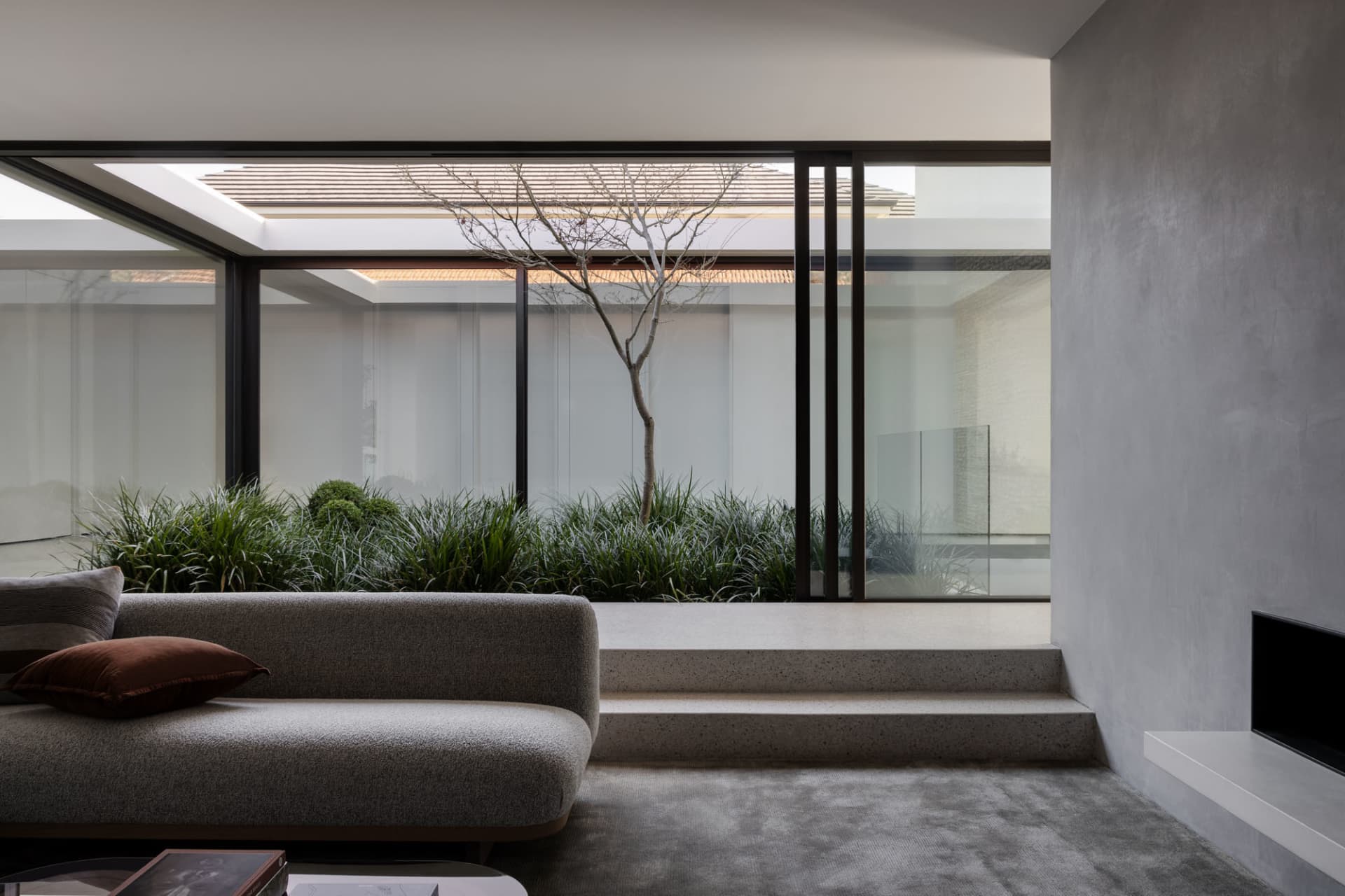A bright and inviting living area with a gray couch, large windows, and potted plants