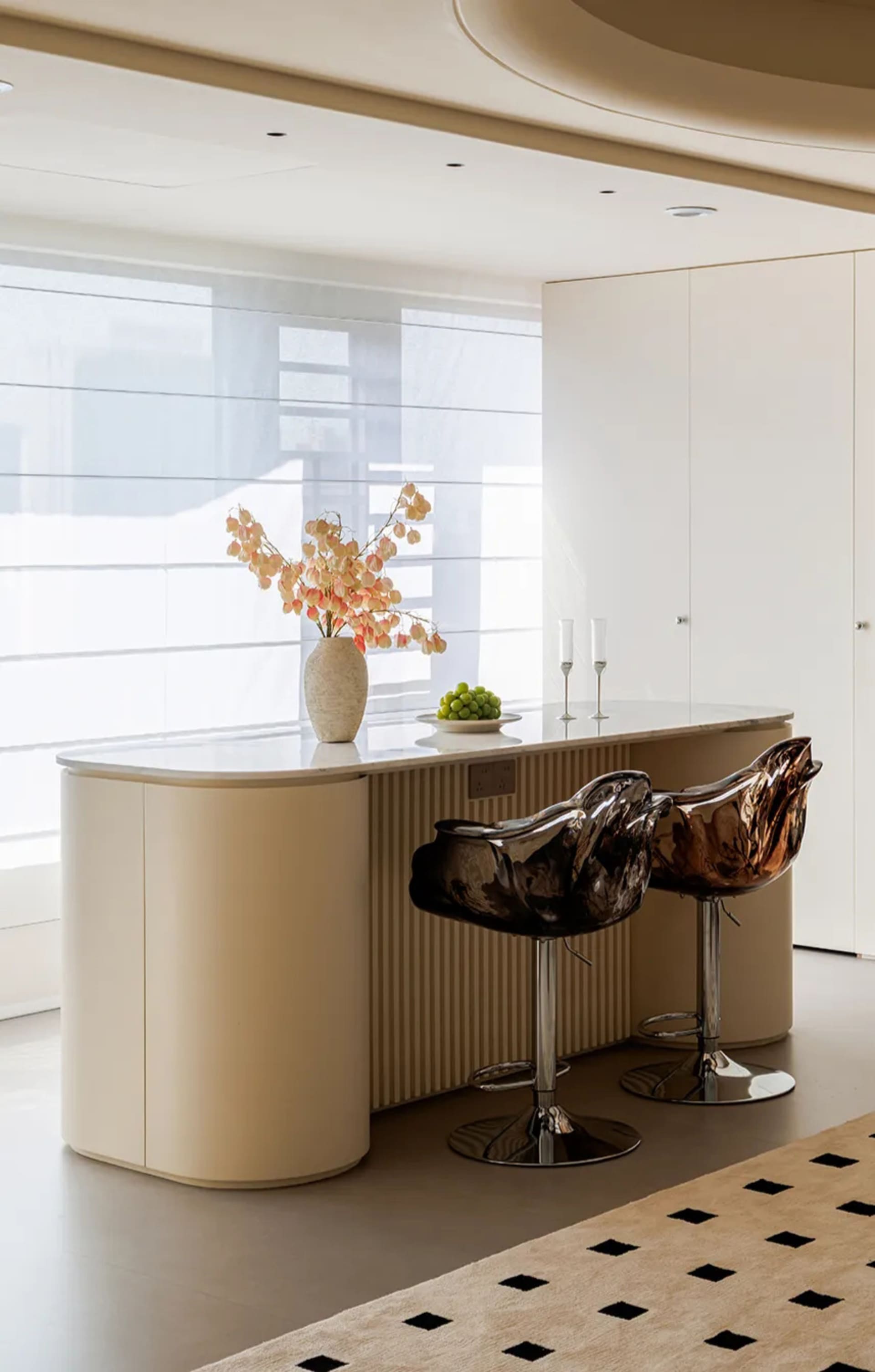 Modern kitchen with white cabinets and countertops, two chairs, a vase with flowers, and wine glasses on the counter