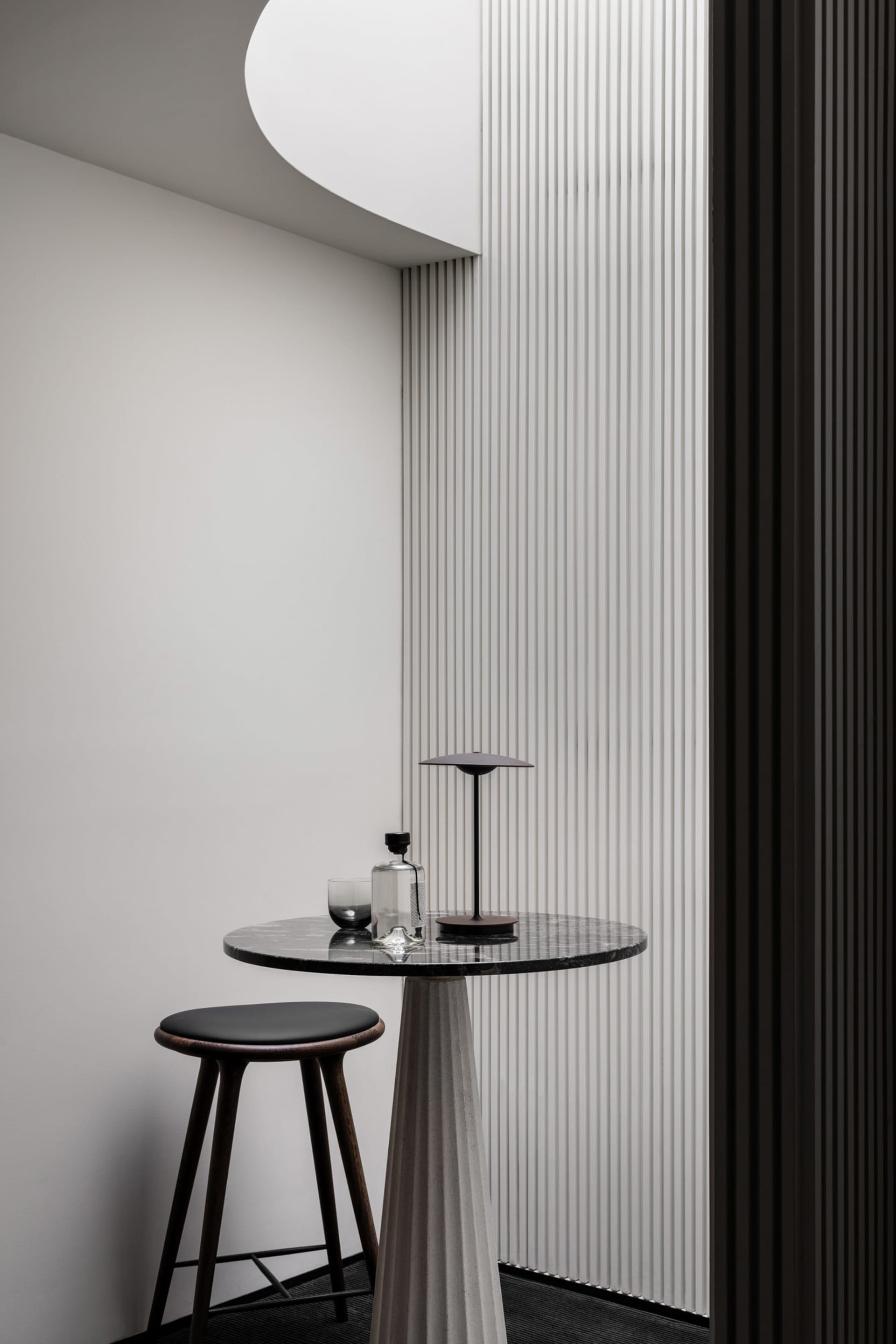 A small table with a vase sits in front of a striped wall, surrounded by two chairs in an elegant and well-organized interior design space