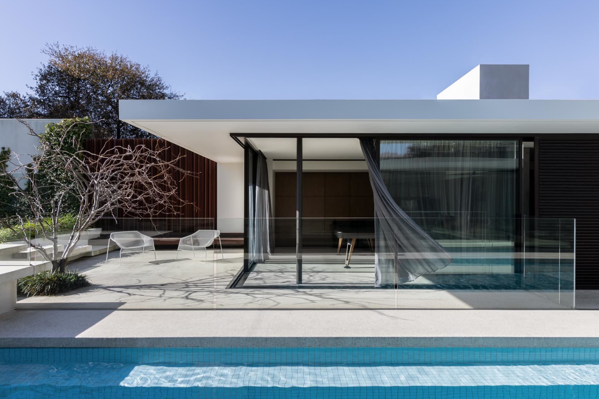 Indoor pool area with a large glass door, clear blue water, and poolside chairs in a relaxing and luxurious environment