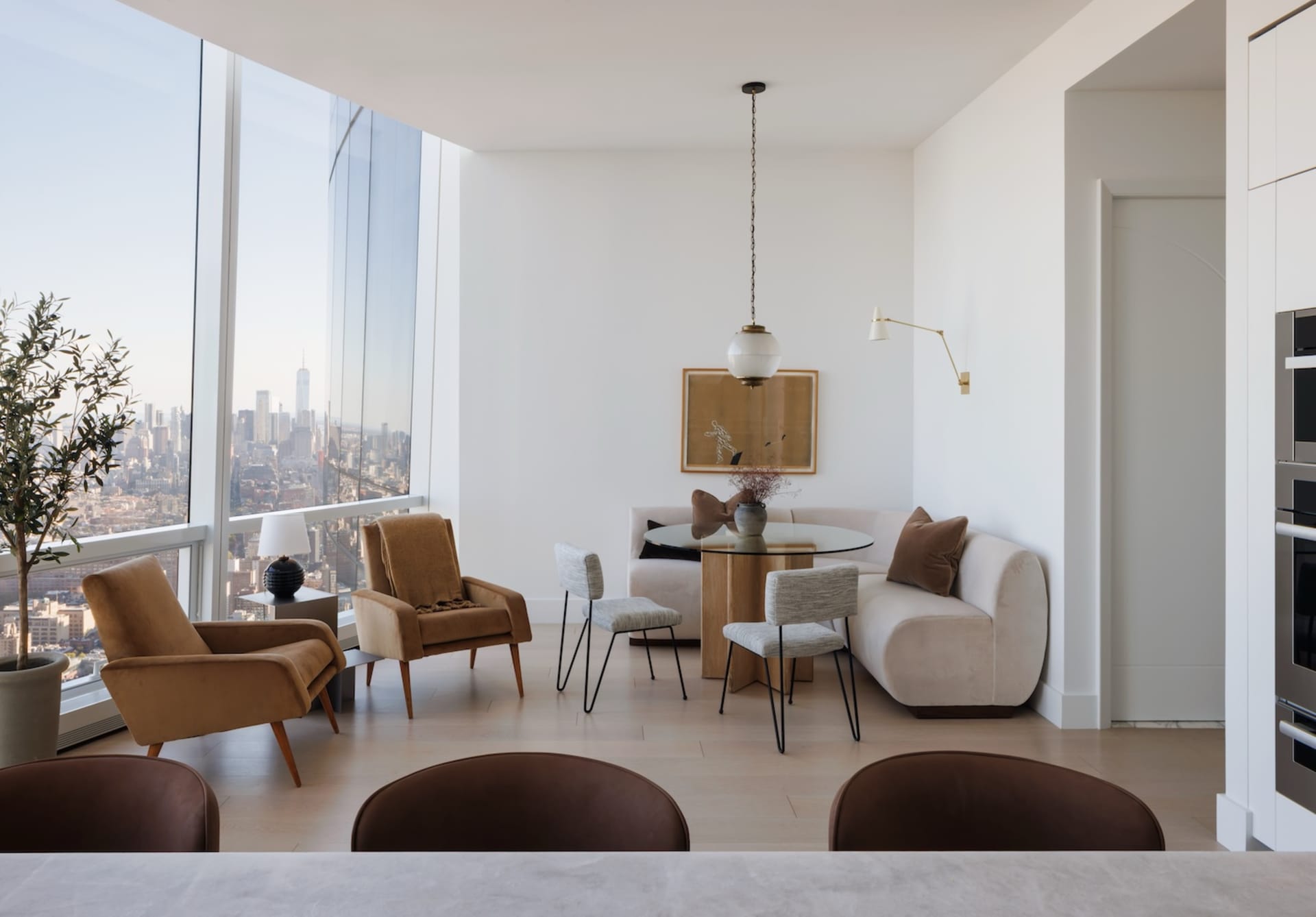 Architectural rendering of a high-rise living room with white walls, hardwood floors, and large windows offering a city view, featuring two couches, chairs, a dining table, and decorative accents
