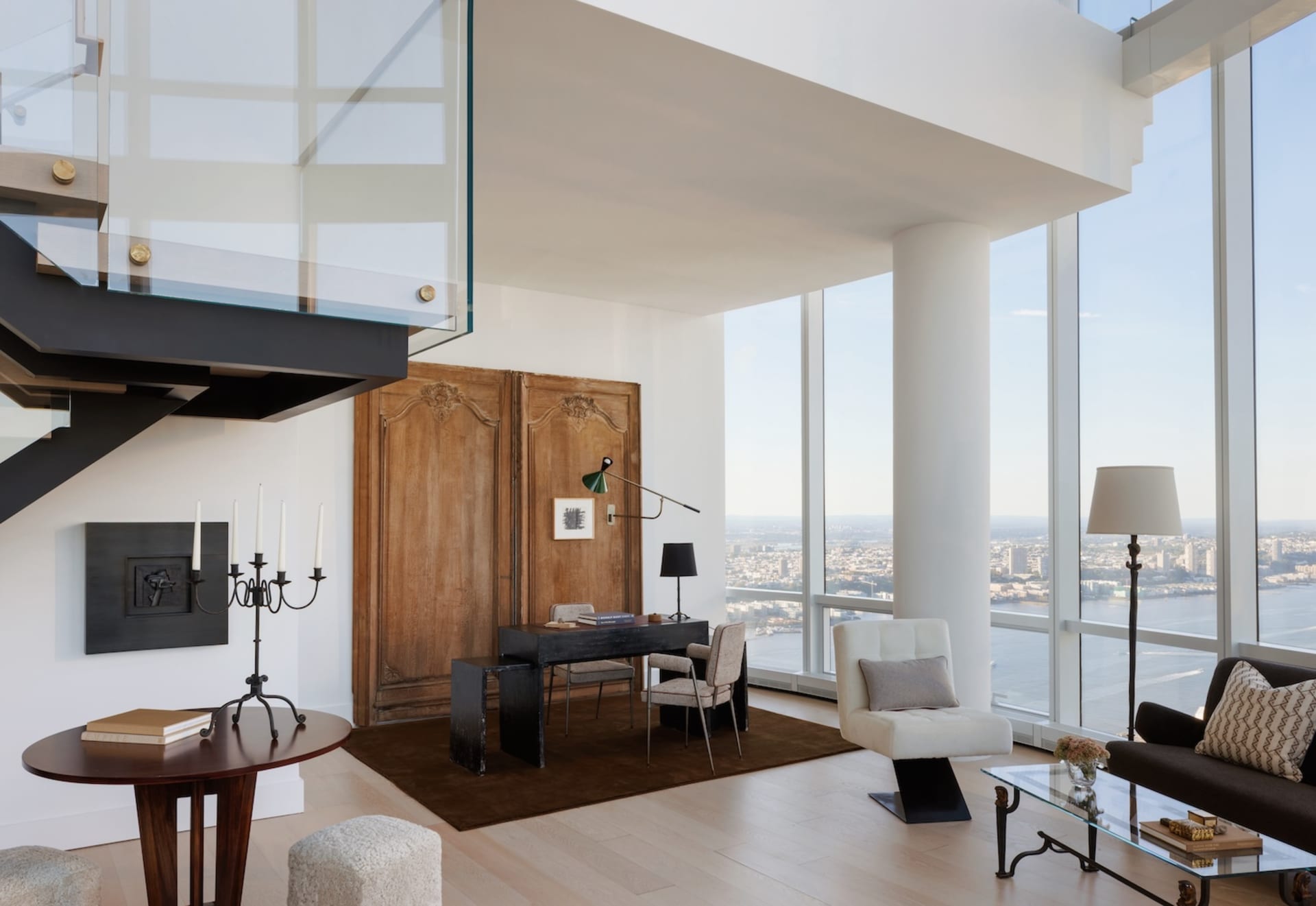 High-rise living room with hardwood floors, large windows, and a city skyline view, featuring a couch, chair, dining table, and bookshelf