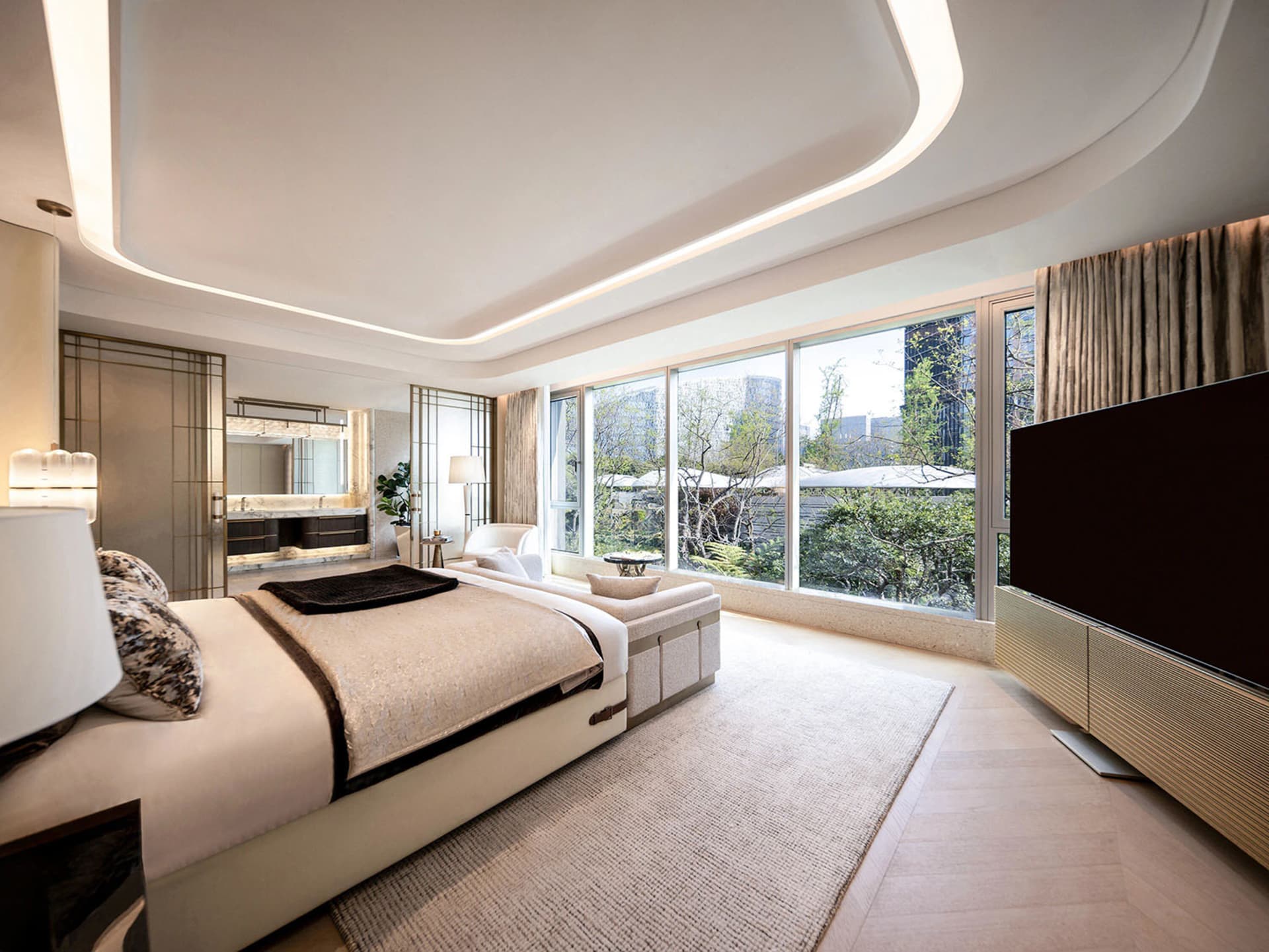 A comfortable living room with a white bed, black headboard, and natural light from windows, surrounded by couches and a TV