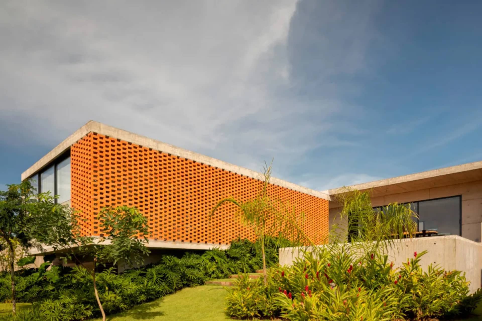 A modern building with a unique orange brick facade, large window, and surrounding potted plants