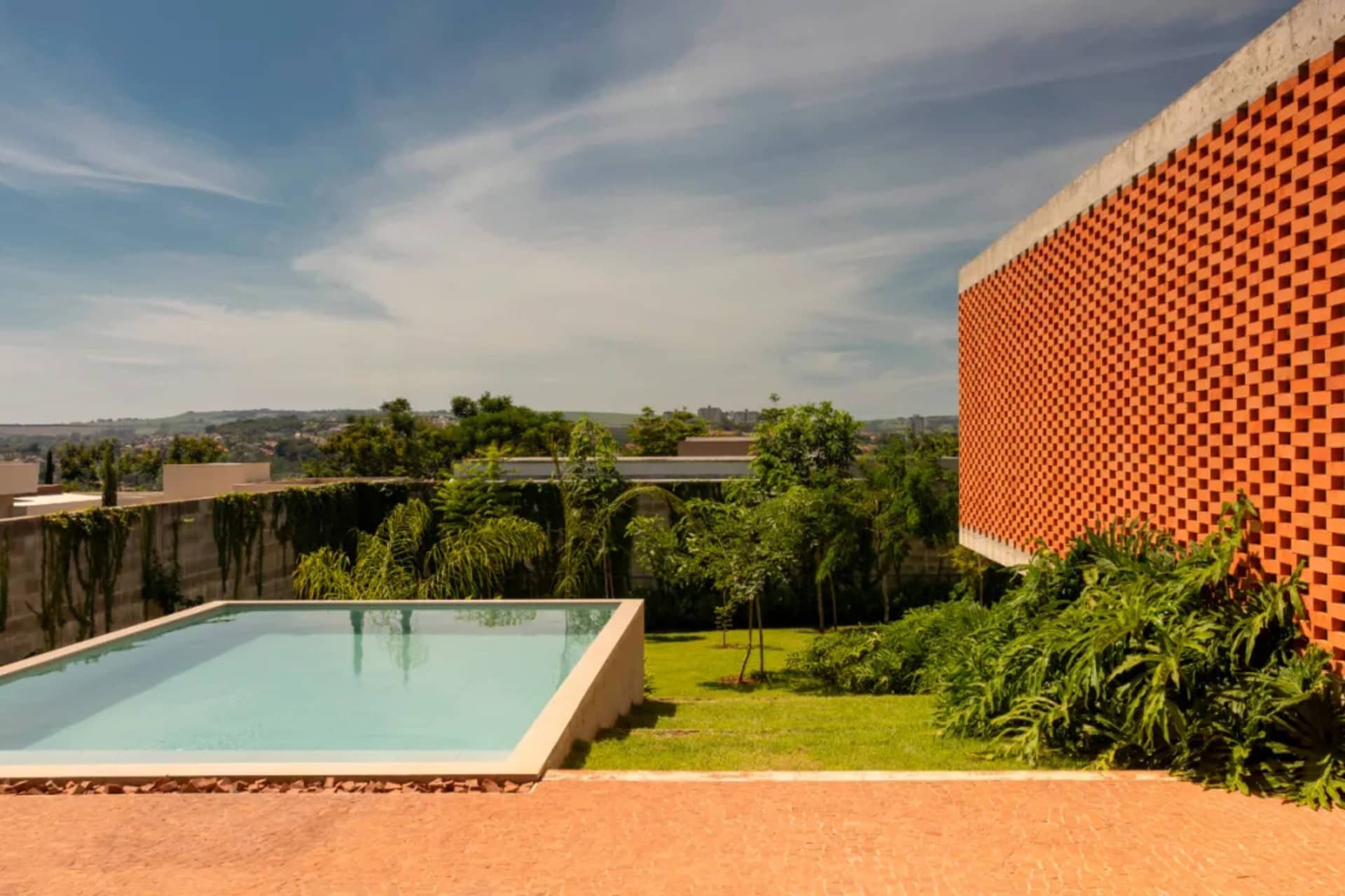 A serene outdoor pool area surrounded by lush greenery and a large building in the background