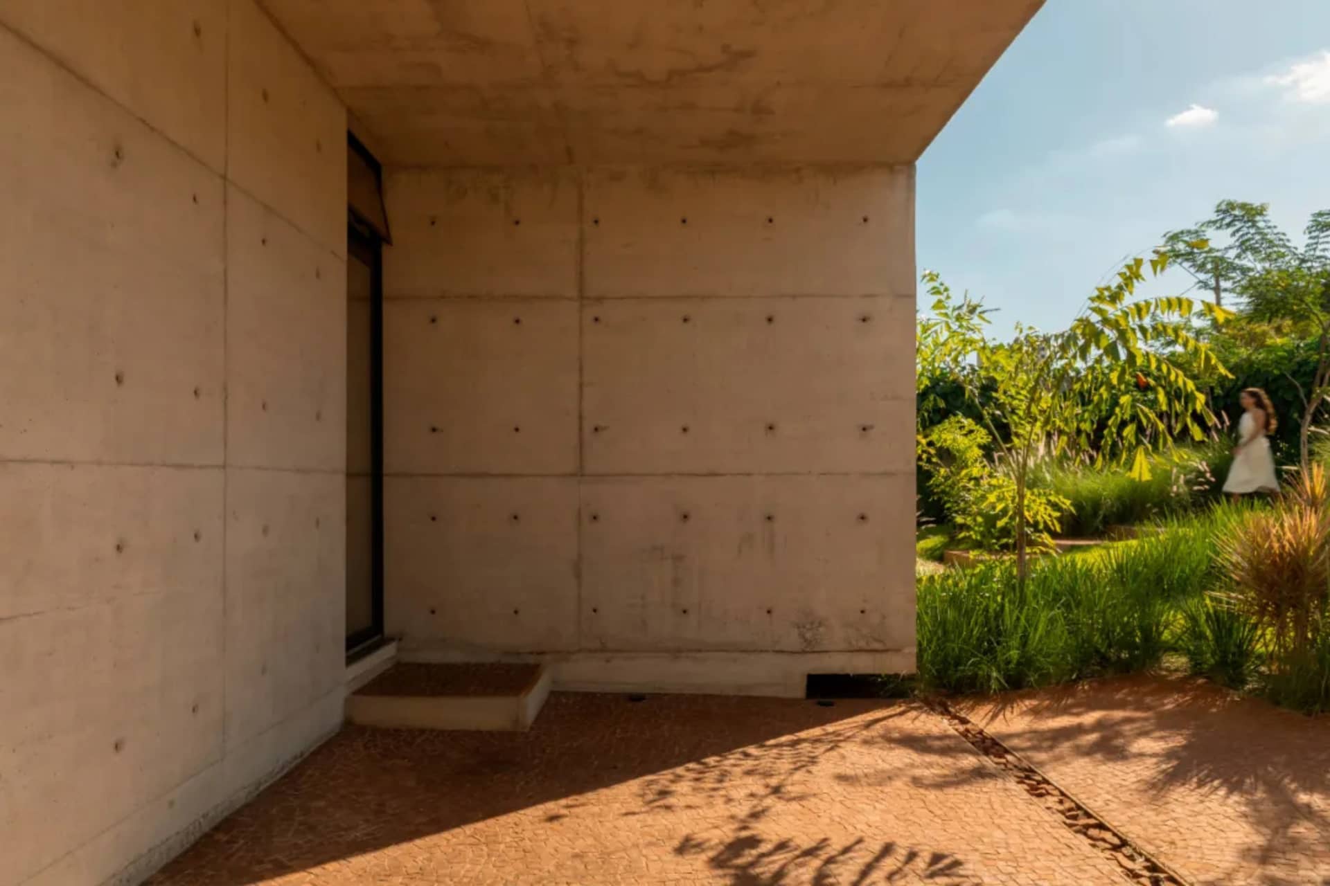 A modern concrete building with a large window on its side, set against a serene background with a tree nearby
