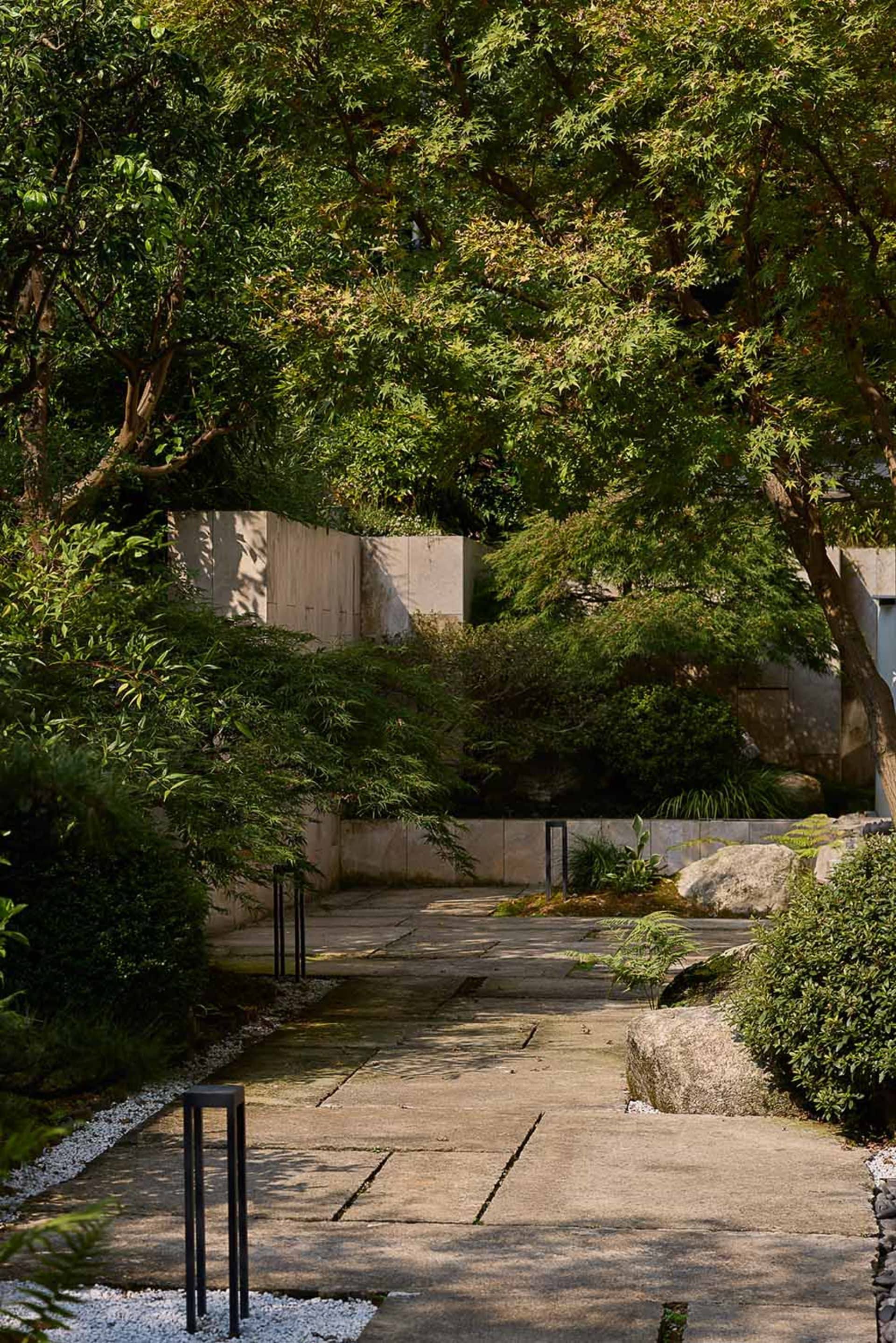 一座傳統石材立面的建築，周圍環繞樹木與灌木叢，營造寧靜氛圍