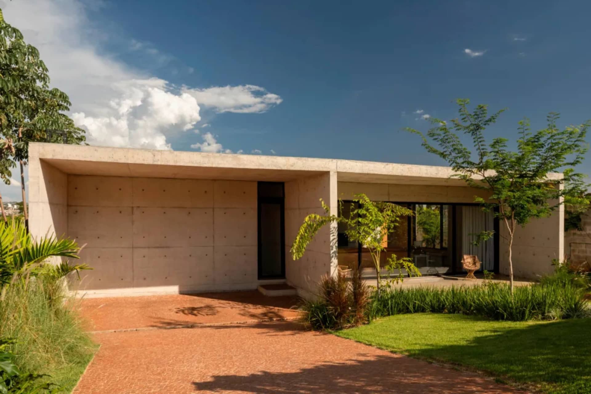 A modern house with a concrete exterior, large windows, and a comfortable living area with several chairs, filled with natural light
