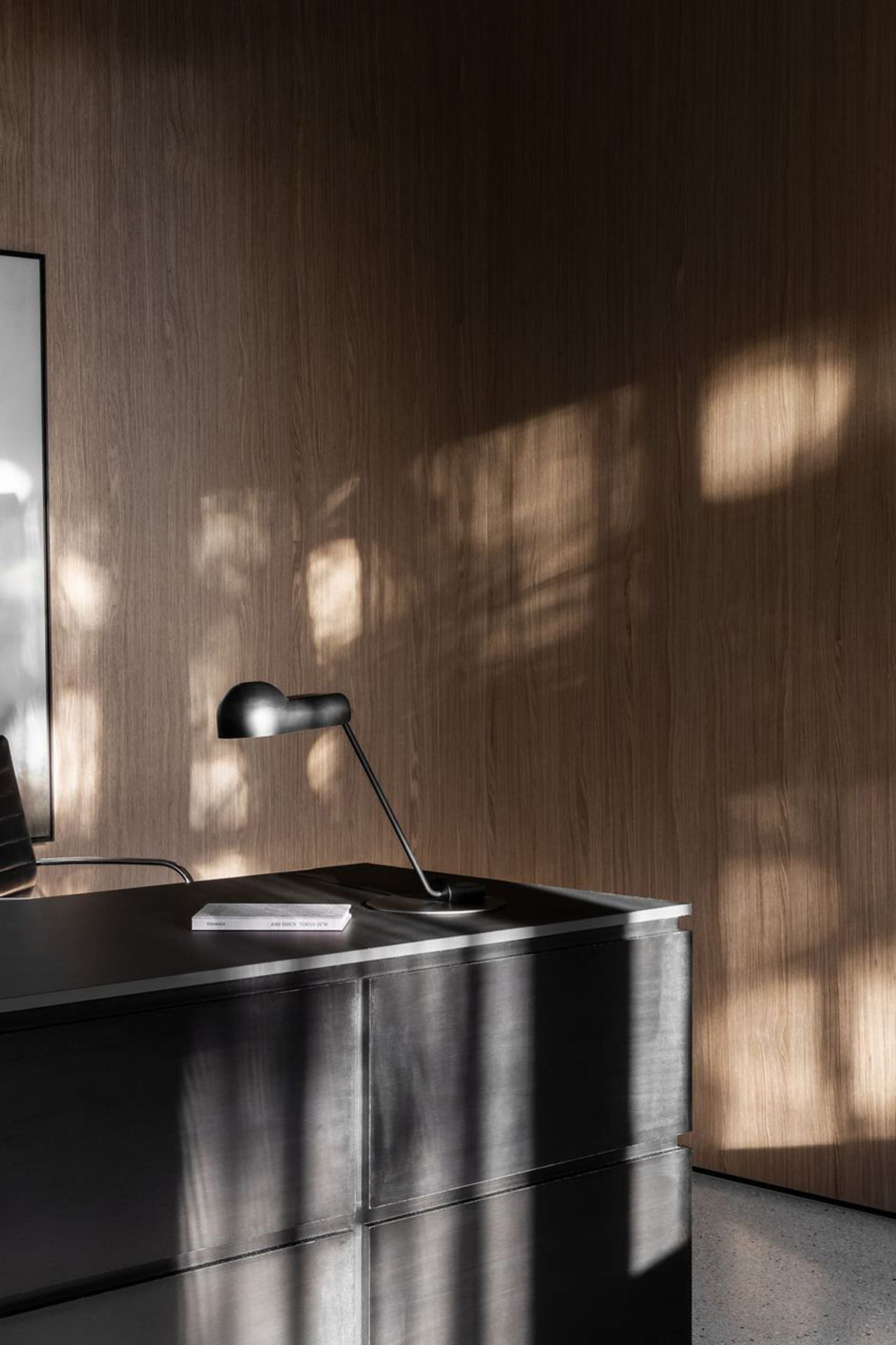 A professional office workspace with a wooden desk, a black chair, and a lamp providing illumination