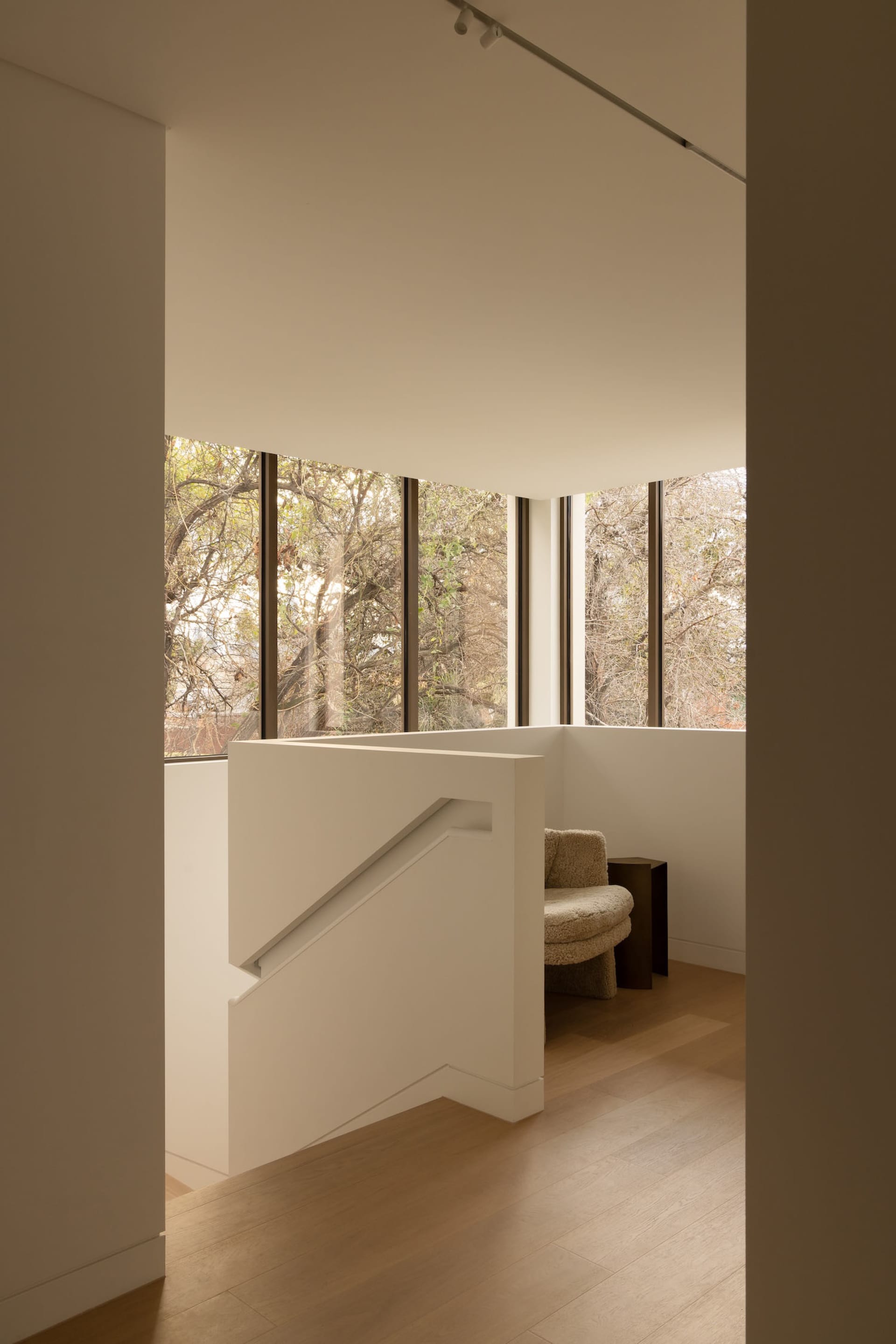A modern living space with white walls, wooden floors, and natural light from two windows, featuring a chair near one of the windows