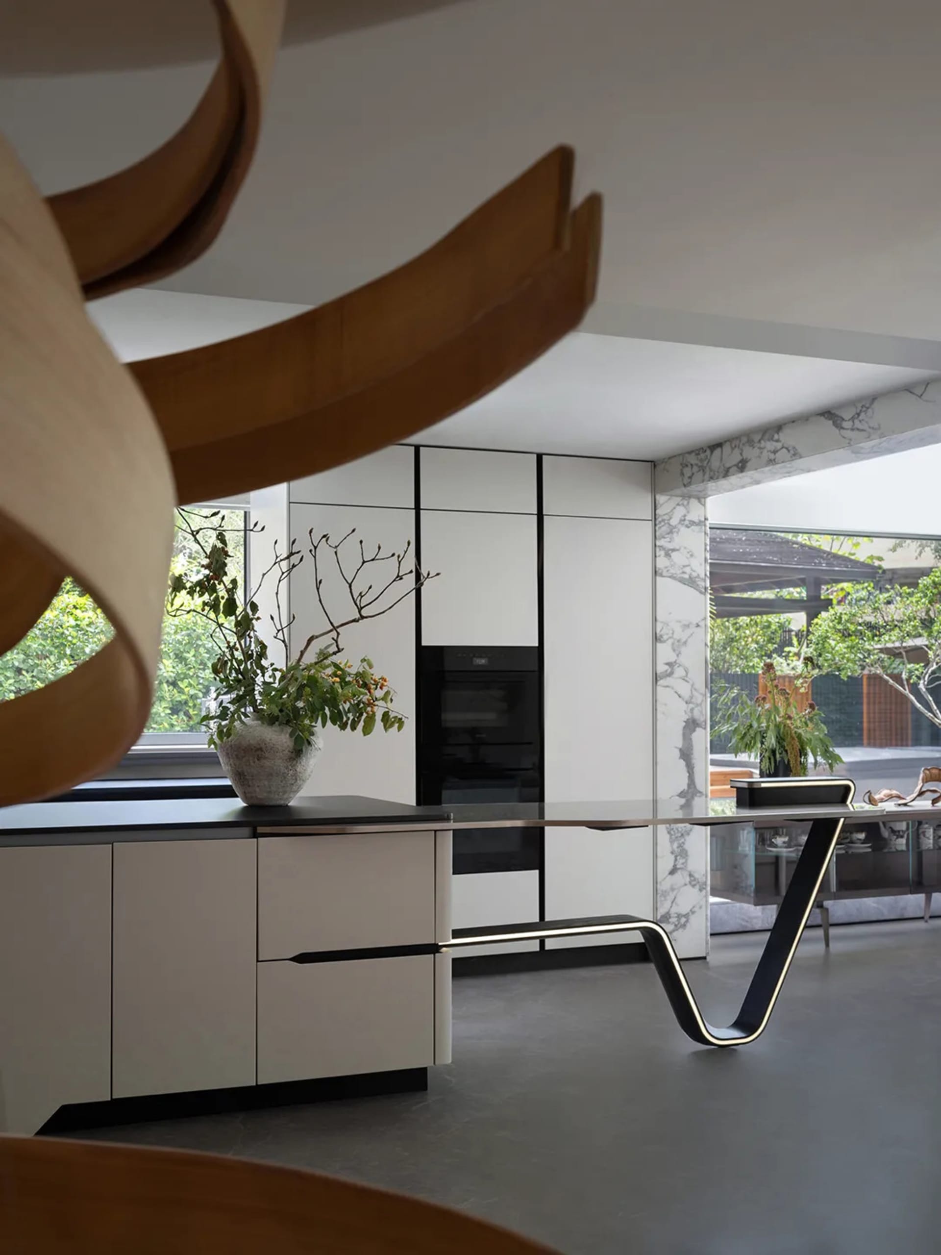 Open kitchen with white cabinets, marble countertops, potted plants, and chairs, near a sink and two ovens