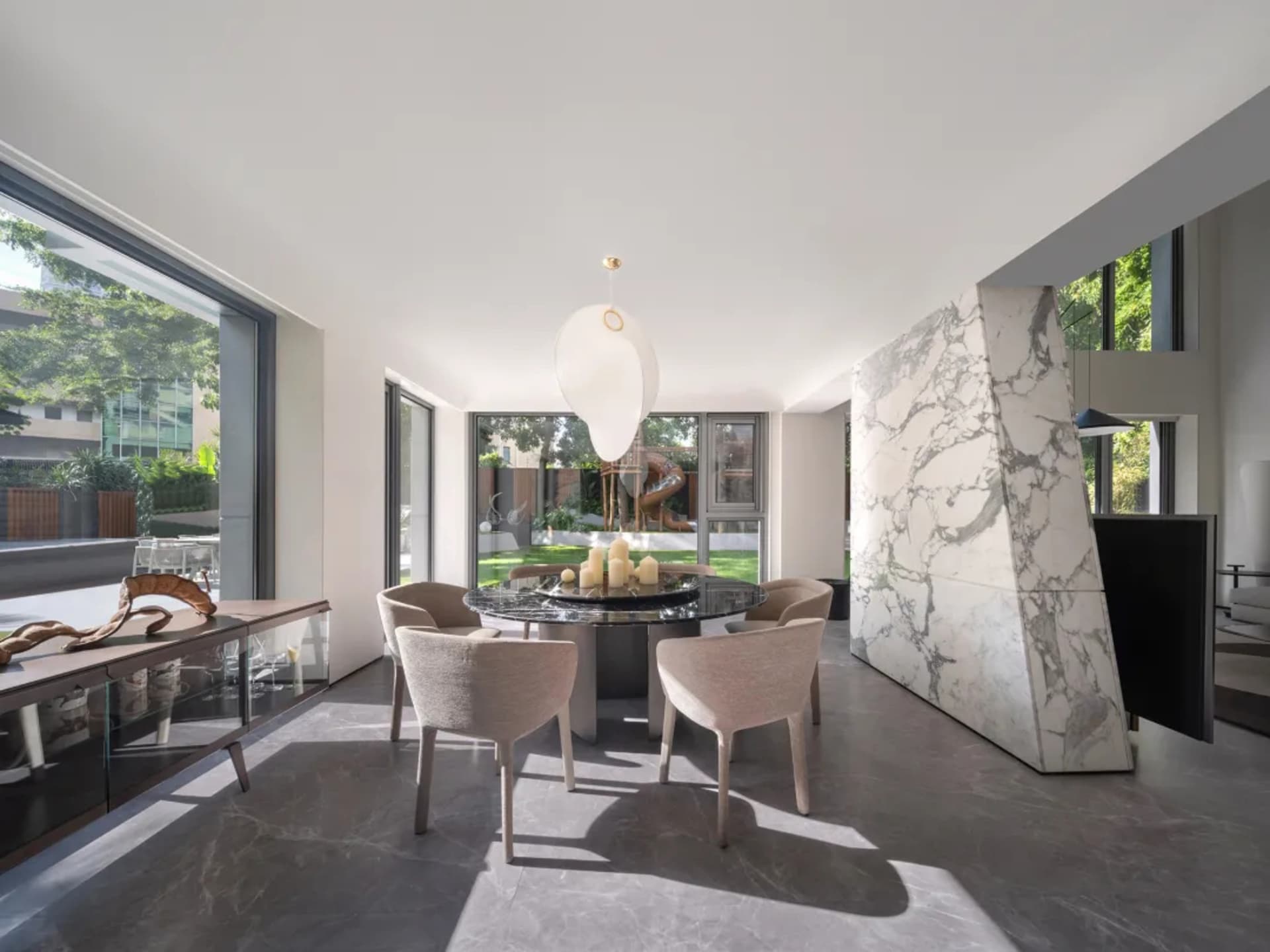 Open modern dining space with a glass-topped dining table surrounded by chairs, a kitchen area with a sink and refrigerator, and a minimalist design