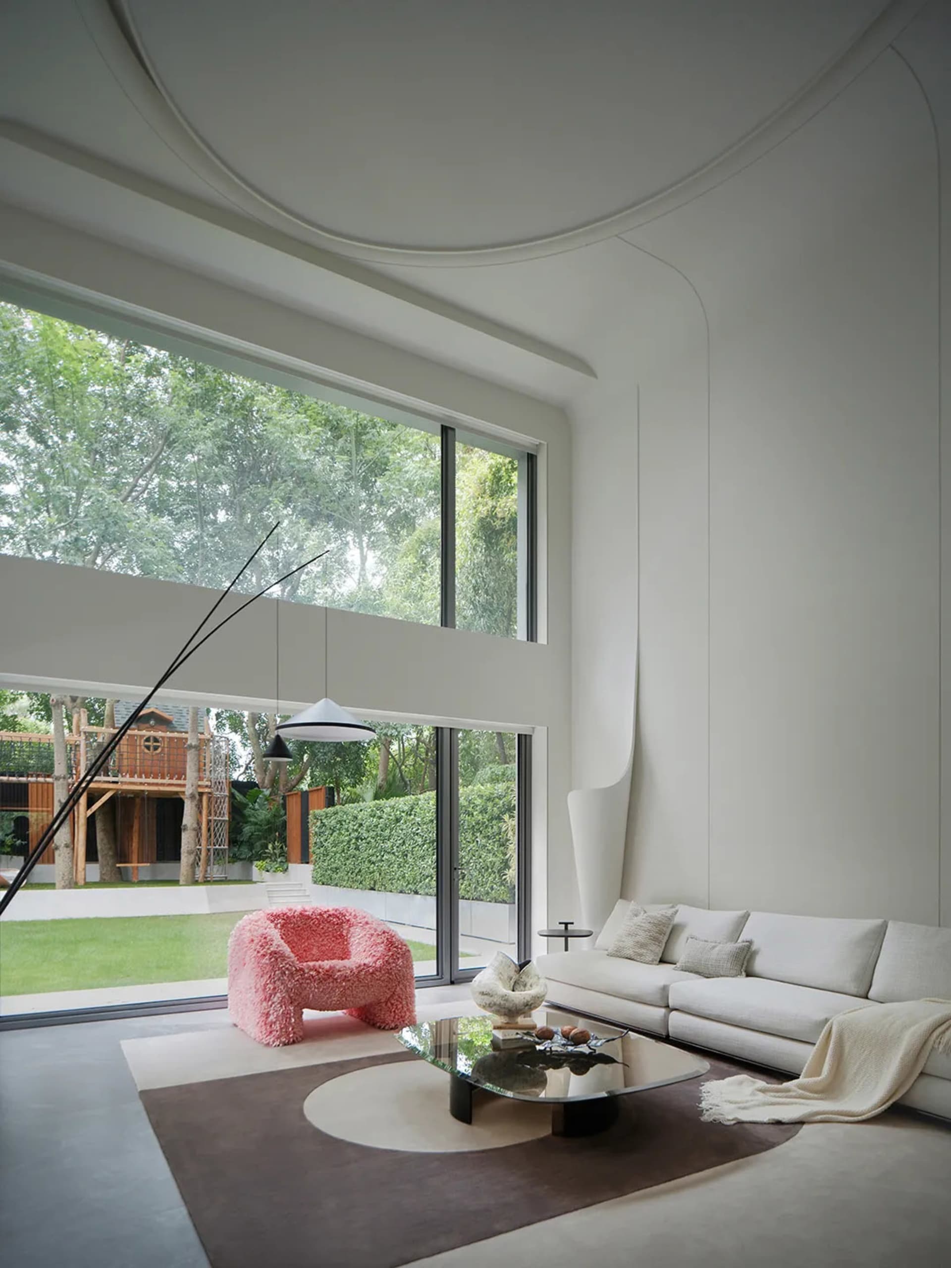 Open modern living space with white walls, a large window, two couches, a dining table, chairs, and a potted plant, filled with natural light