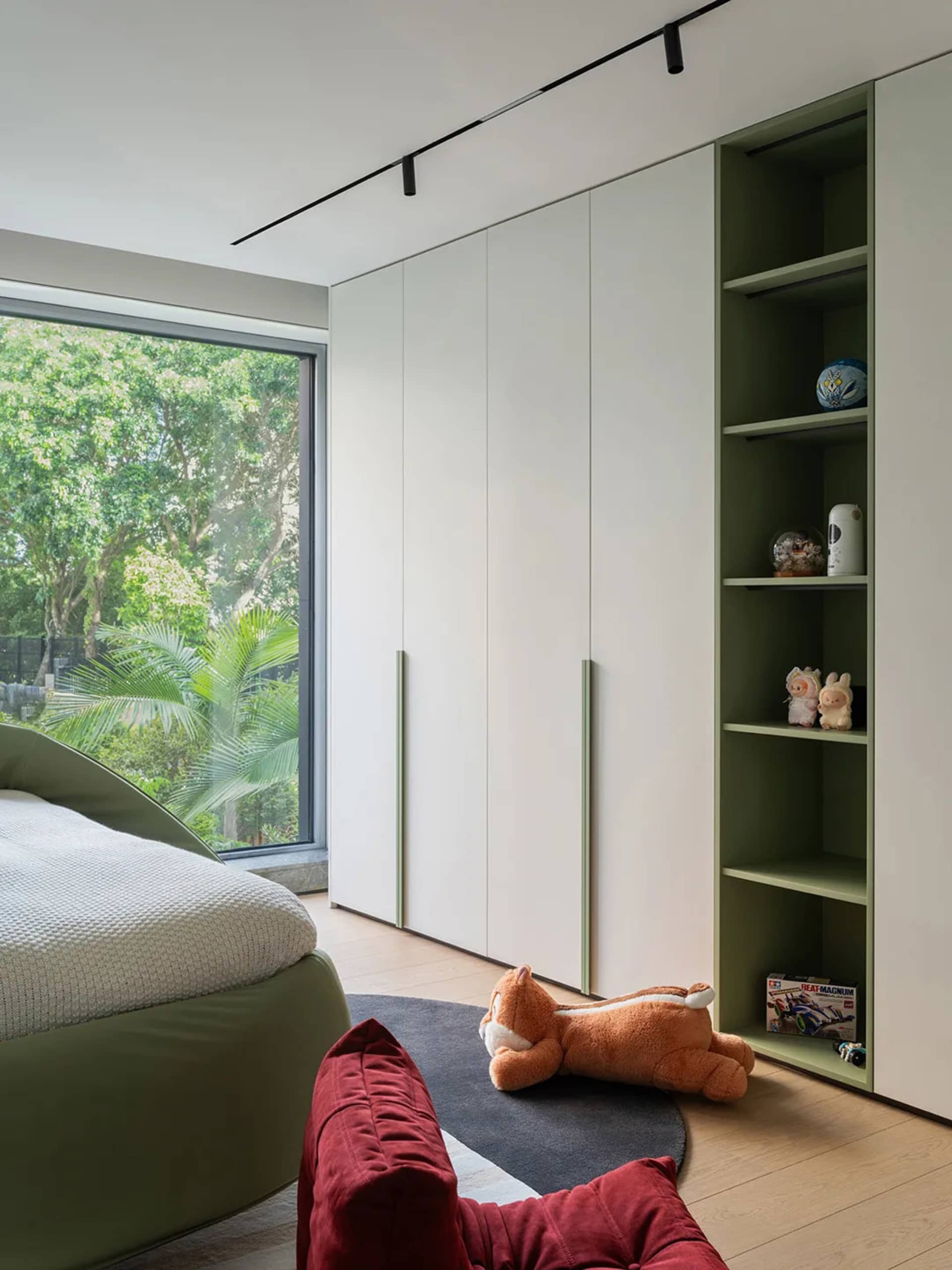 Cozy bedroom with a large bed, a chair, and two teddy bears, featuring a green theme and natural light from the window
