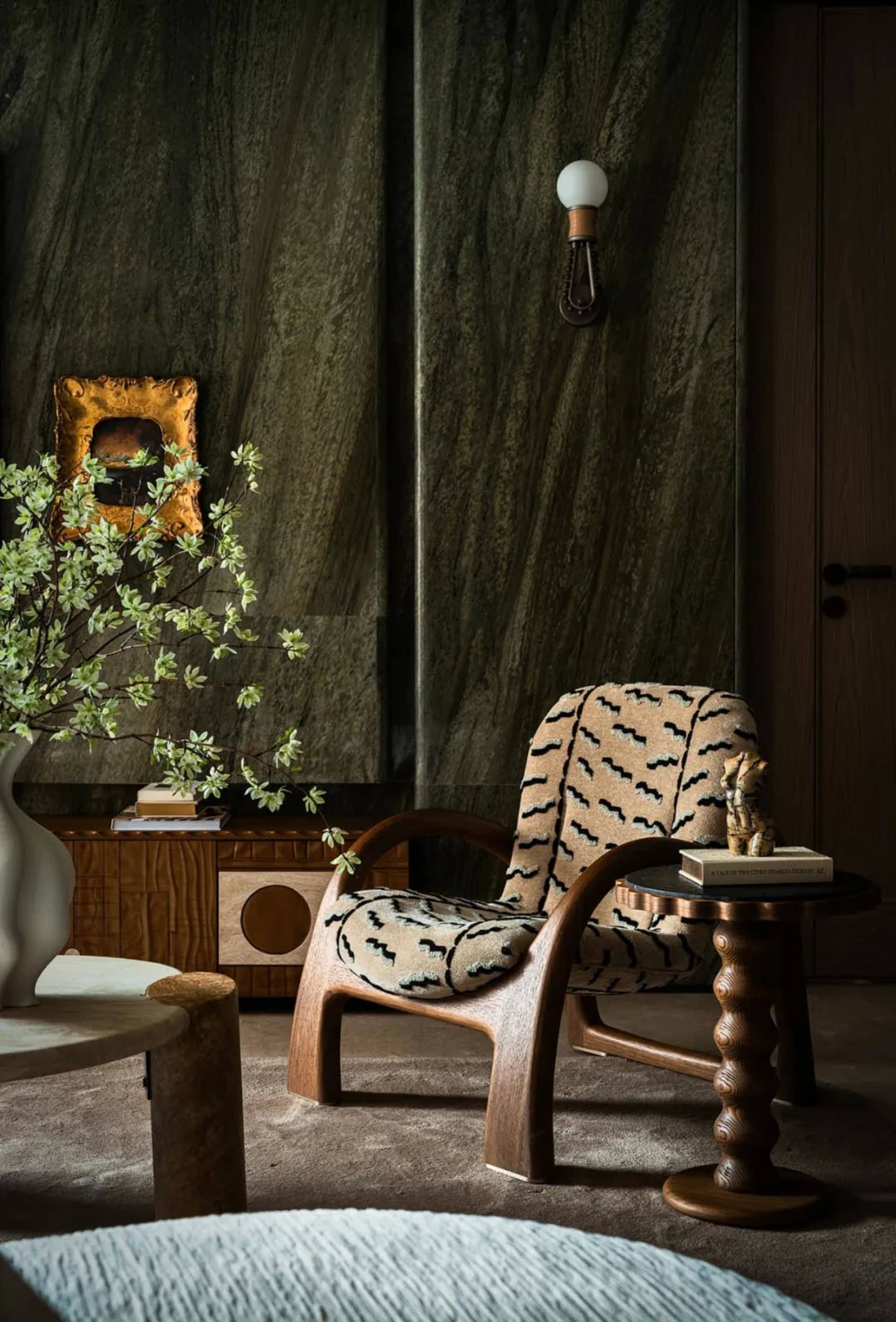 Cozy interior space with a wooden chair, black and white striped chair, stone wall, vases, and a book, featuring natural materials and inviting atmosphere