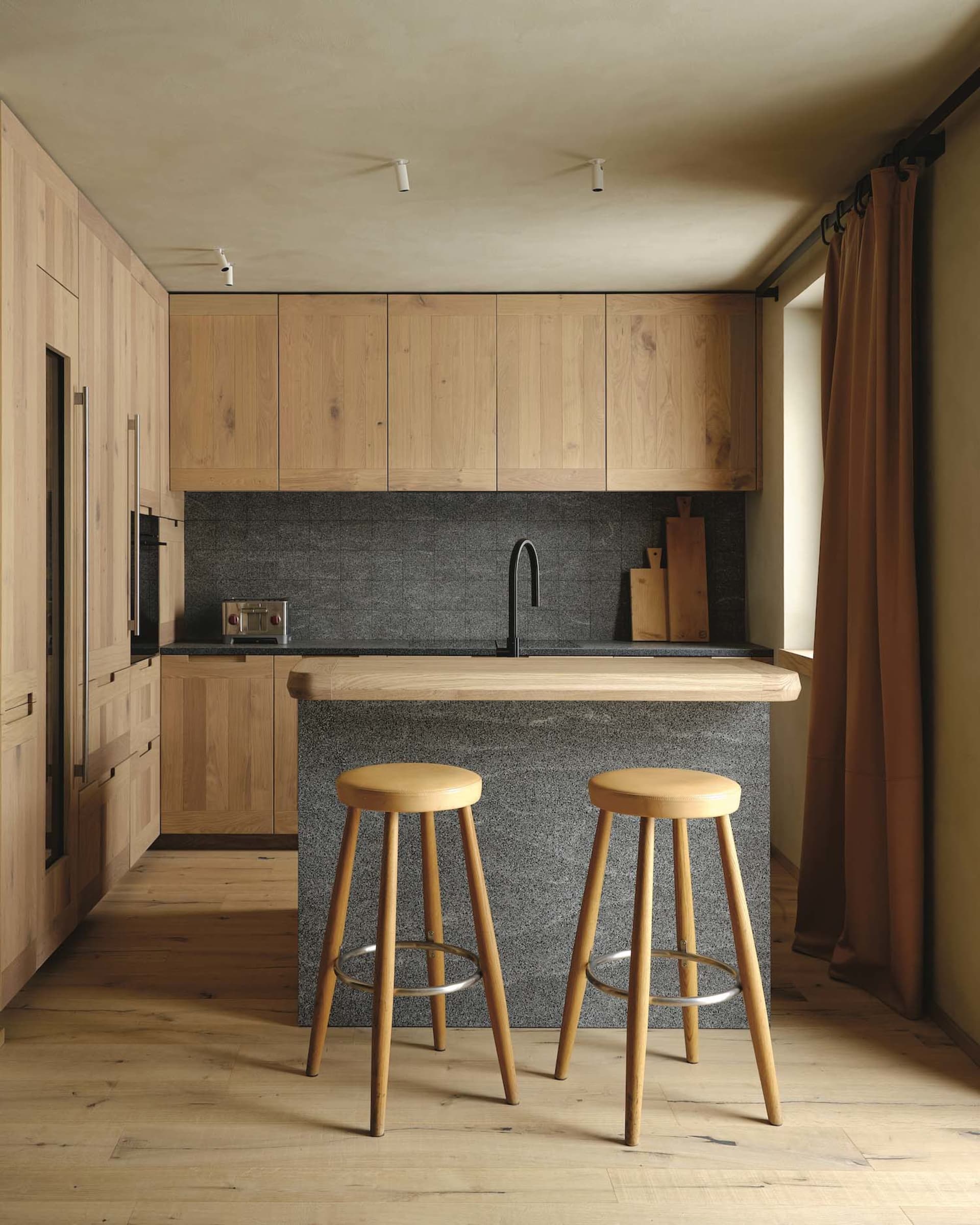Warm kitchen with wooden cabinets, two sinks, and stools for casual dining