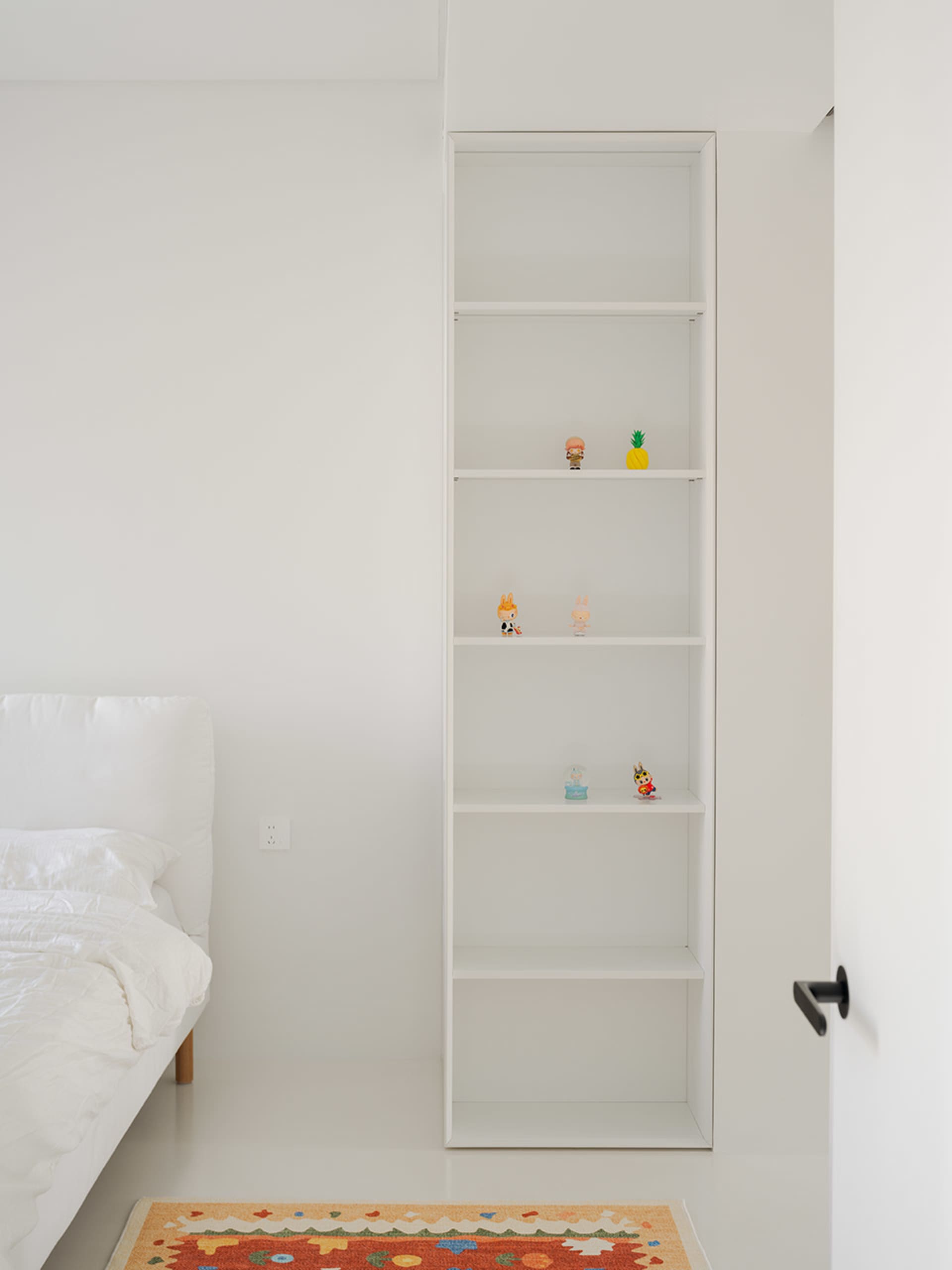 A well-organized bedroom with a large bookshelf filled with books, figurines, and decorative objects, creating an inviting atmosphere