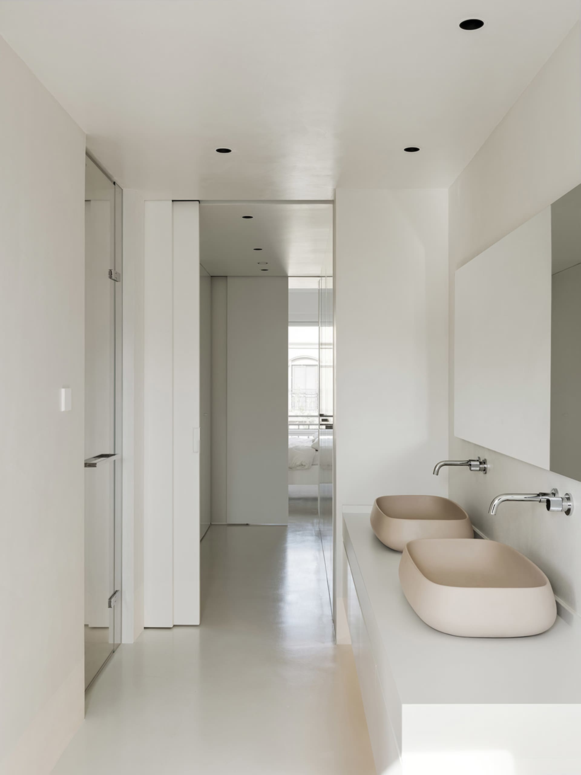 Modern bathroom with two sinks on a white countertop, surrounded by white walls and floors, creating a bright and airy atmosphere