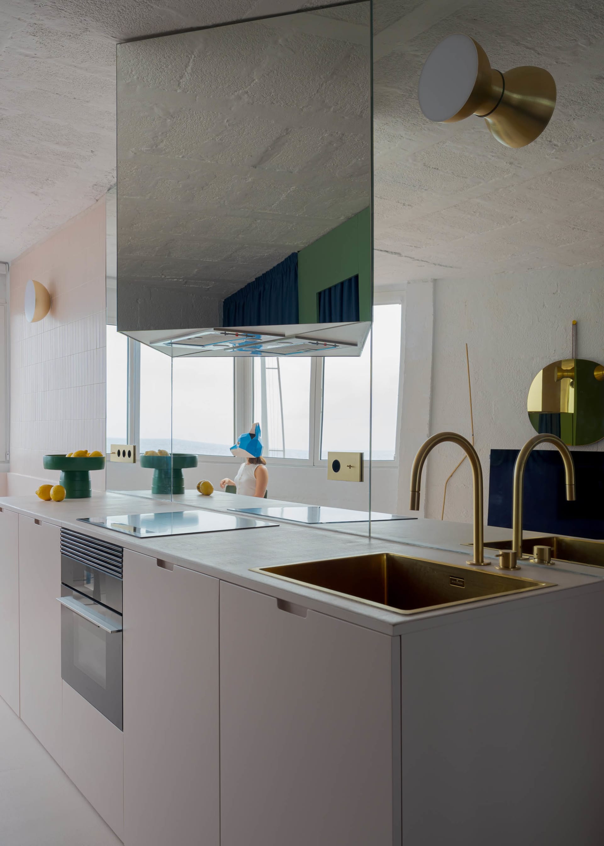 A modern kitchen with white cabinets, a large mirror above the sink, and fruits such as apples and oranges on the countertop