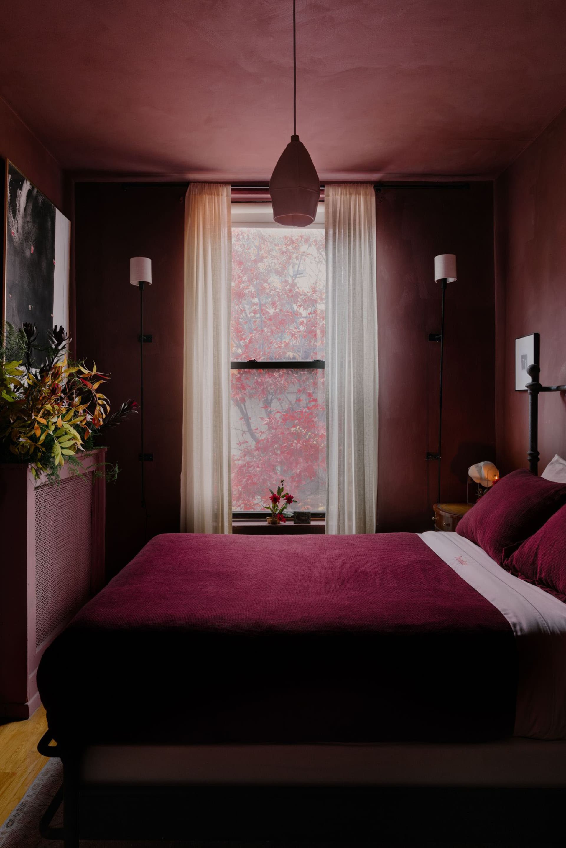 Cozy bedroom with a large bed, red walls, potted plants, and a vase, creating a warm and inviting atmosphere