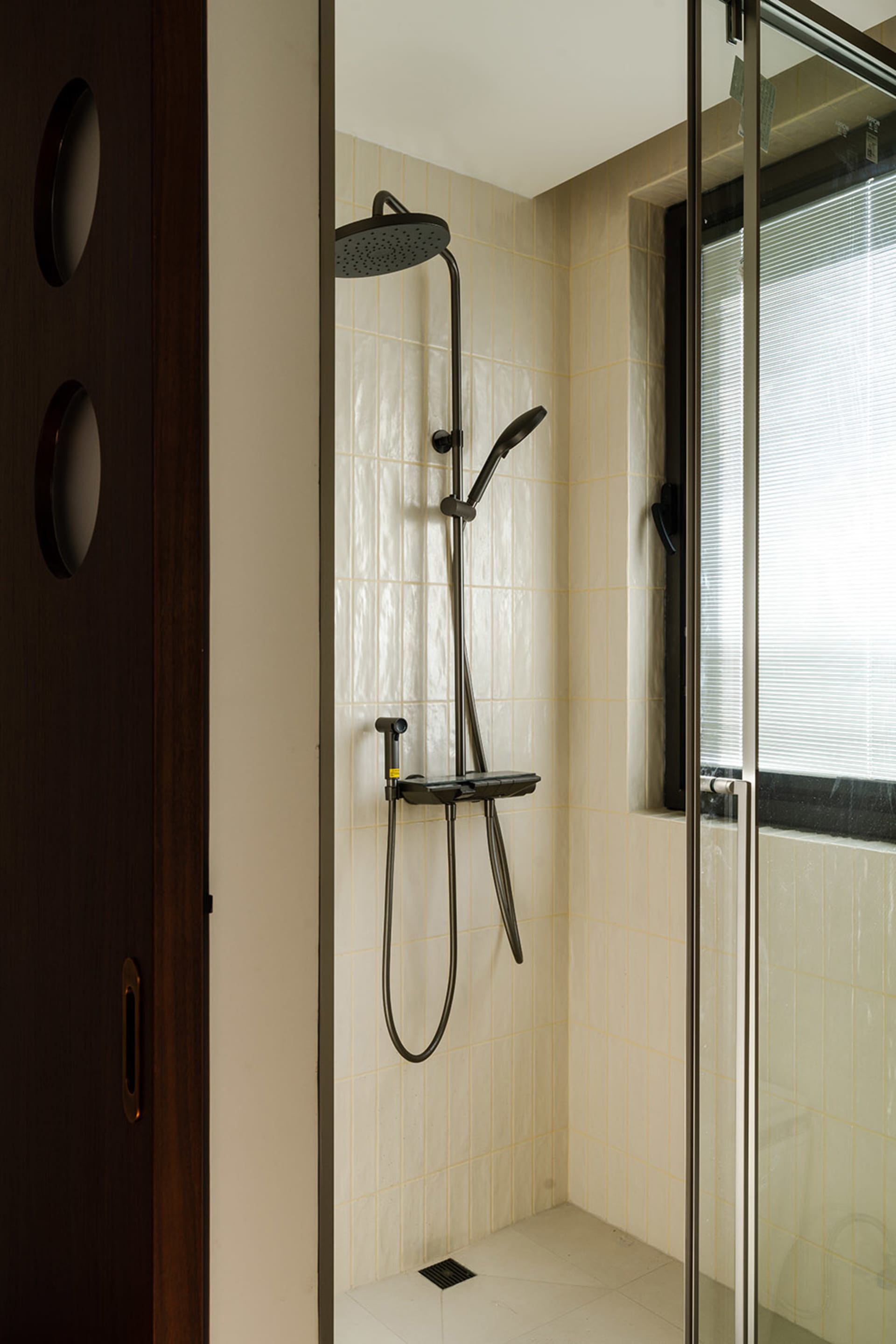 Bathroom with a tile shower, black shower head, and silver pole, featuring natural light from a window