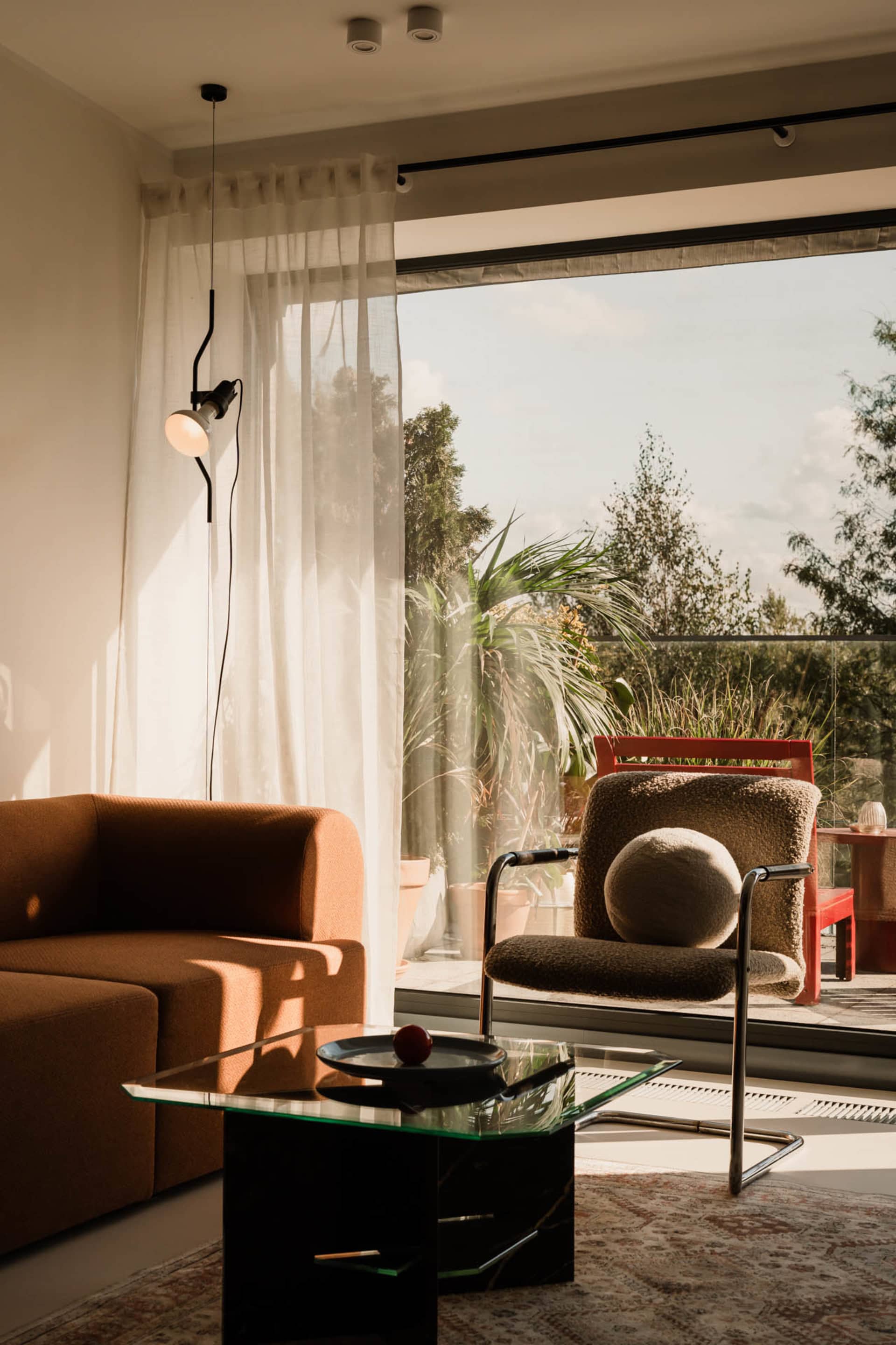 Cozy living area with a couch, chair, and dining table, featuring a red seat, natural light, and a potted plant