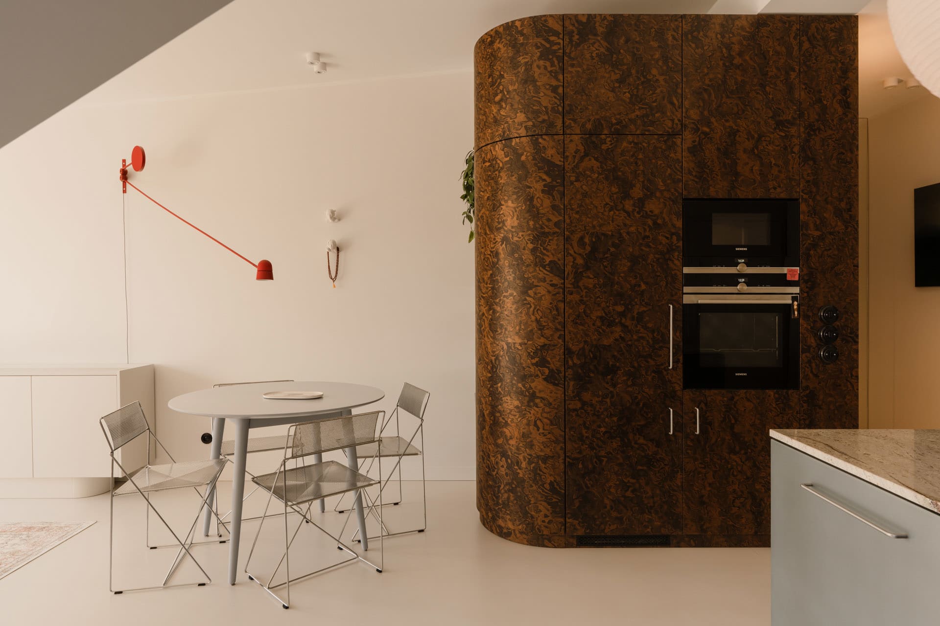 Open kitchen area with wooden cabinets, a large brown cabinet, and two dining tables with chairs, a potted plant adding greenery to the space