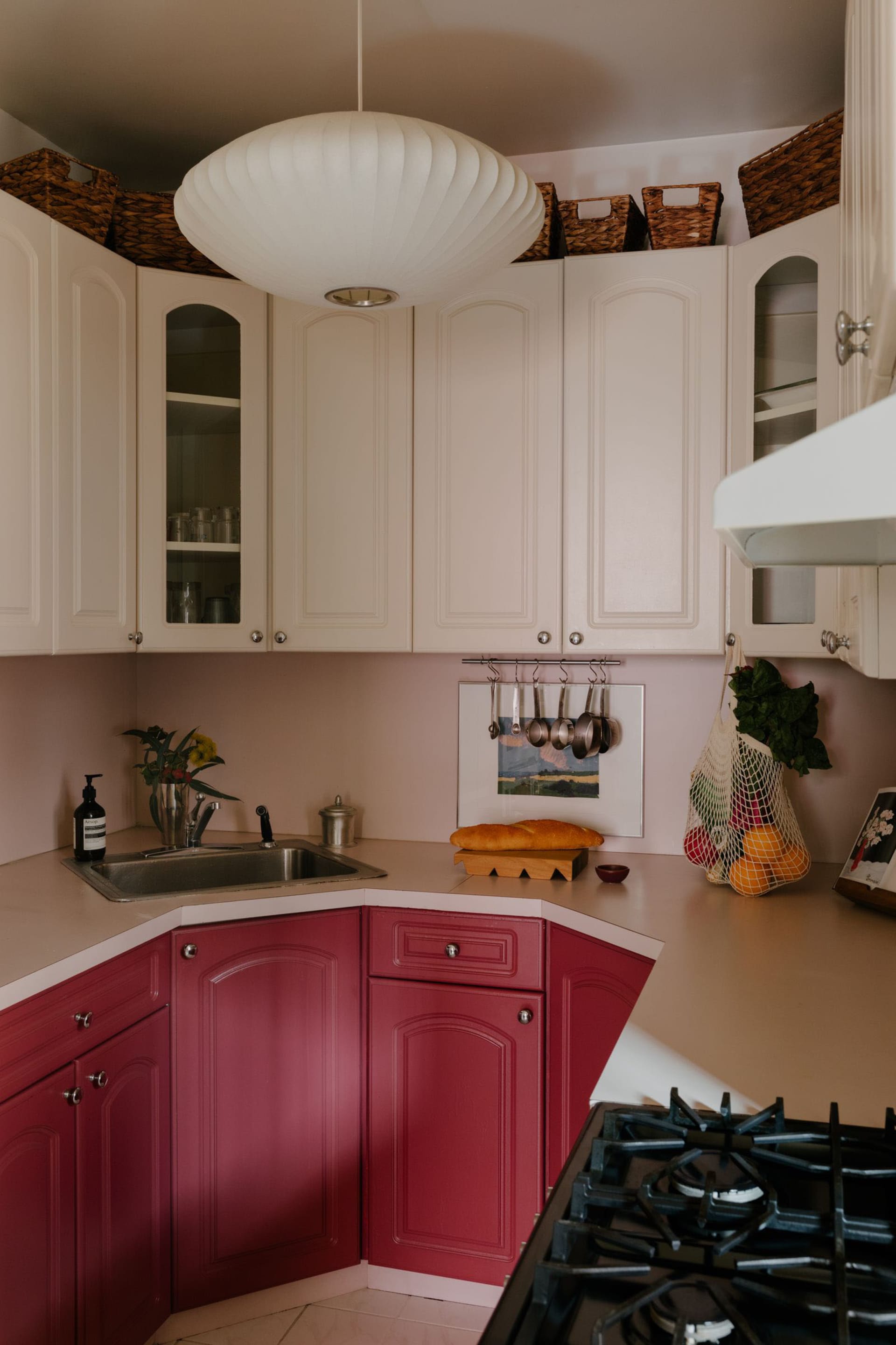 Warm and inviting kitchen with pink cabinets, white walls, and kitchen essentials like a sink, oven, and bowls