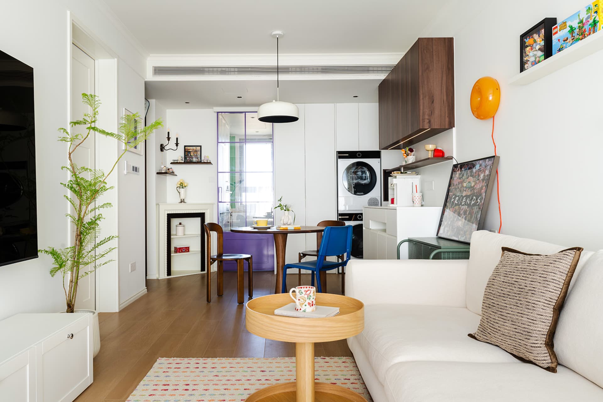 Modern living room, kitchen, and dining area with white walls, a couch, refrigerator, oven, sink, and dining table