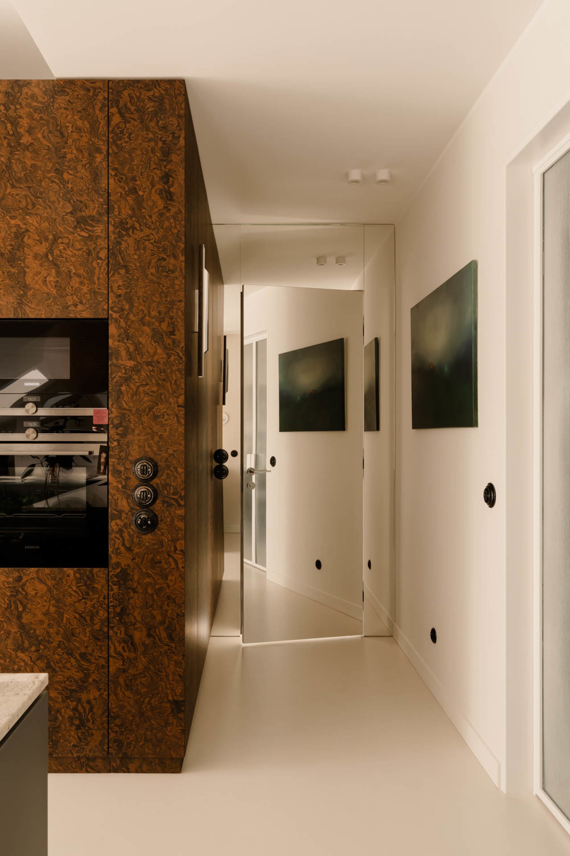 A clean and bright hallway with white walls and flooring, featuring three framed pictures and a microwave near one of the doors