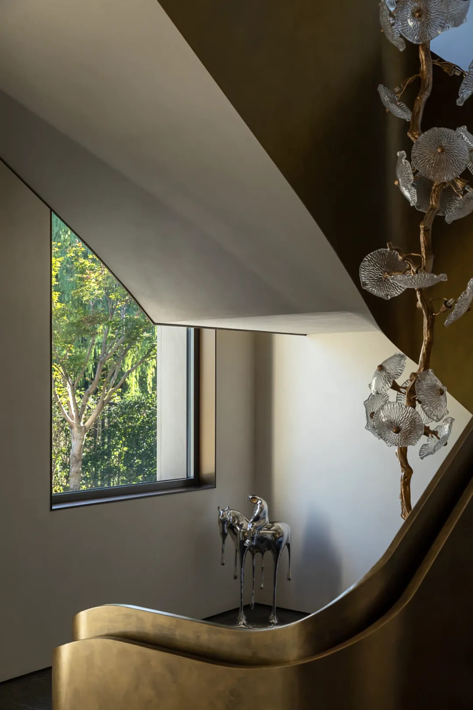 A calm and inviting interior space with a staircase, white wall, and window, featuring two statues at the base of the stairs